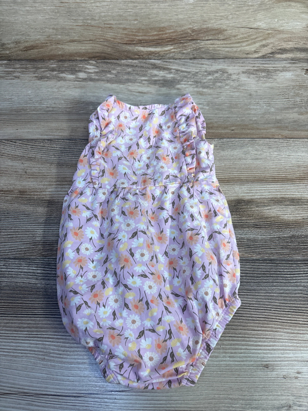 Top down view of Minymo pink floral bubble romper with ruffle sleeves and elastic leg openings on light wood background