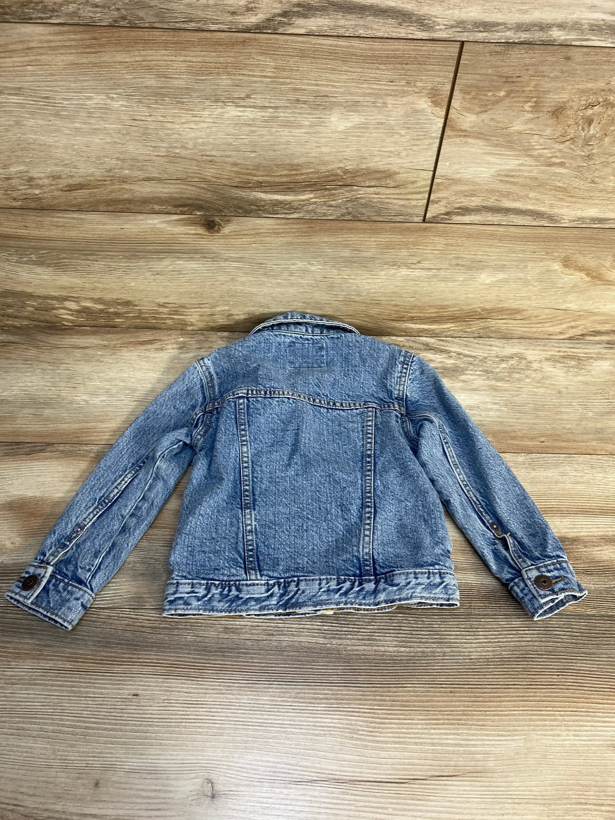 Children's denim jean jacket laid flat on wood floor, back view, kids outerwear resale