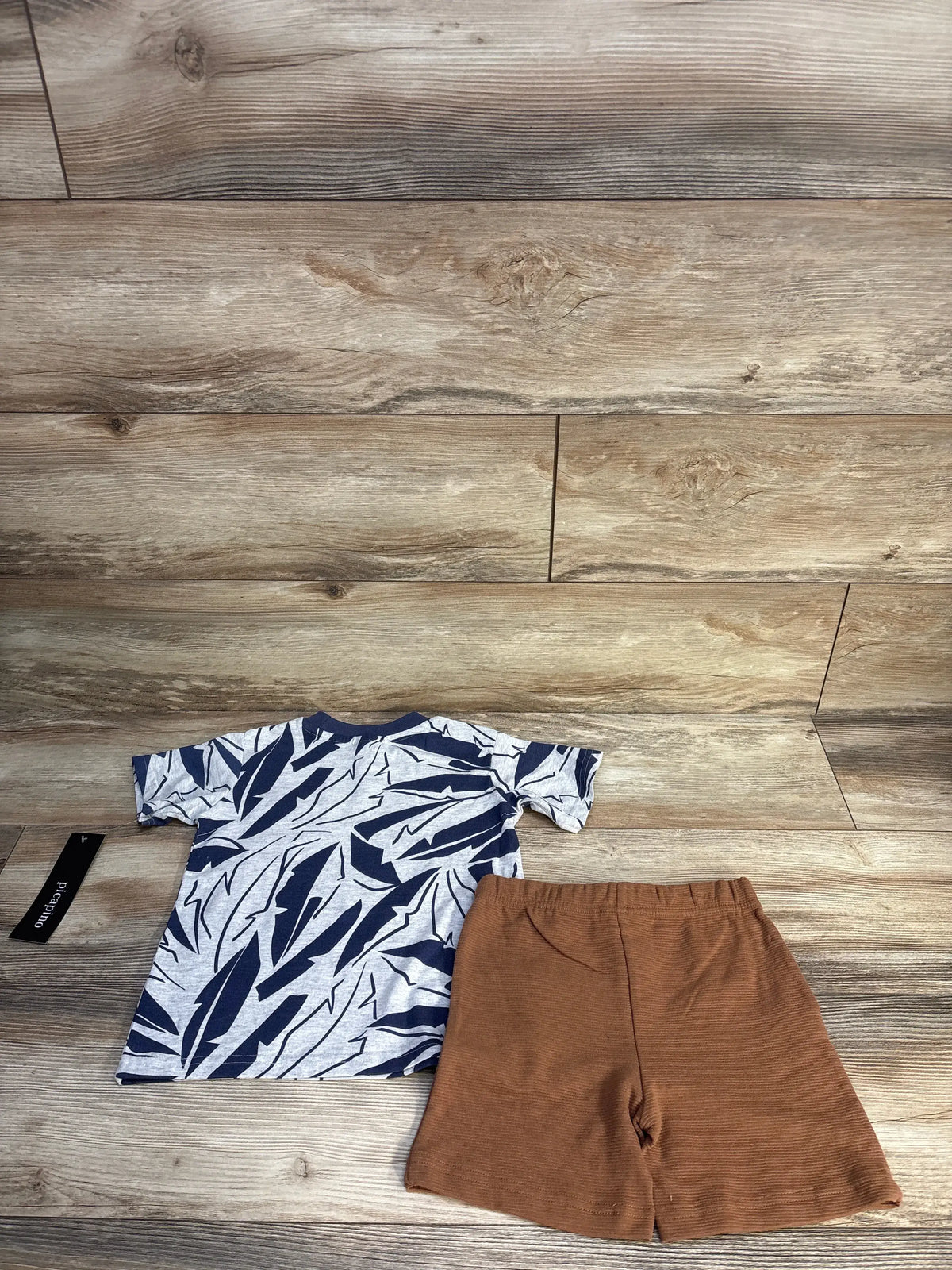 Top-down view of Picapino navy shirt and shorts set with abstract leaf-print shirt and elastic waist shorts on wood flooring