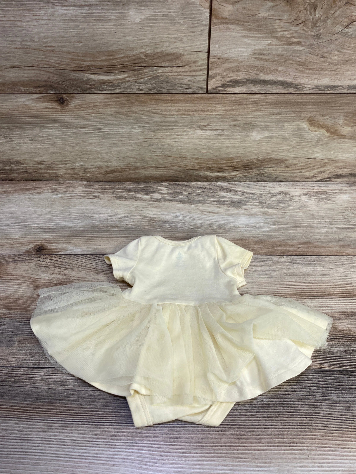 Top view of Disney Baby Winnie the Pooh yellow newborn tutu bodysuit showcasing its layered tulle skirt on a wood background