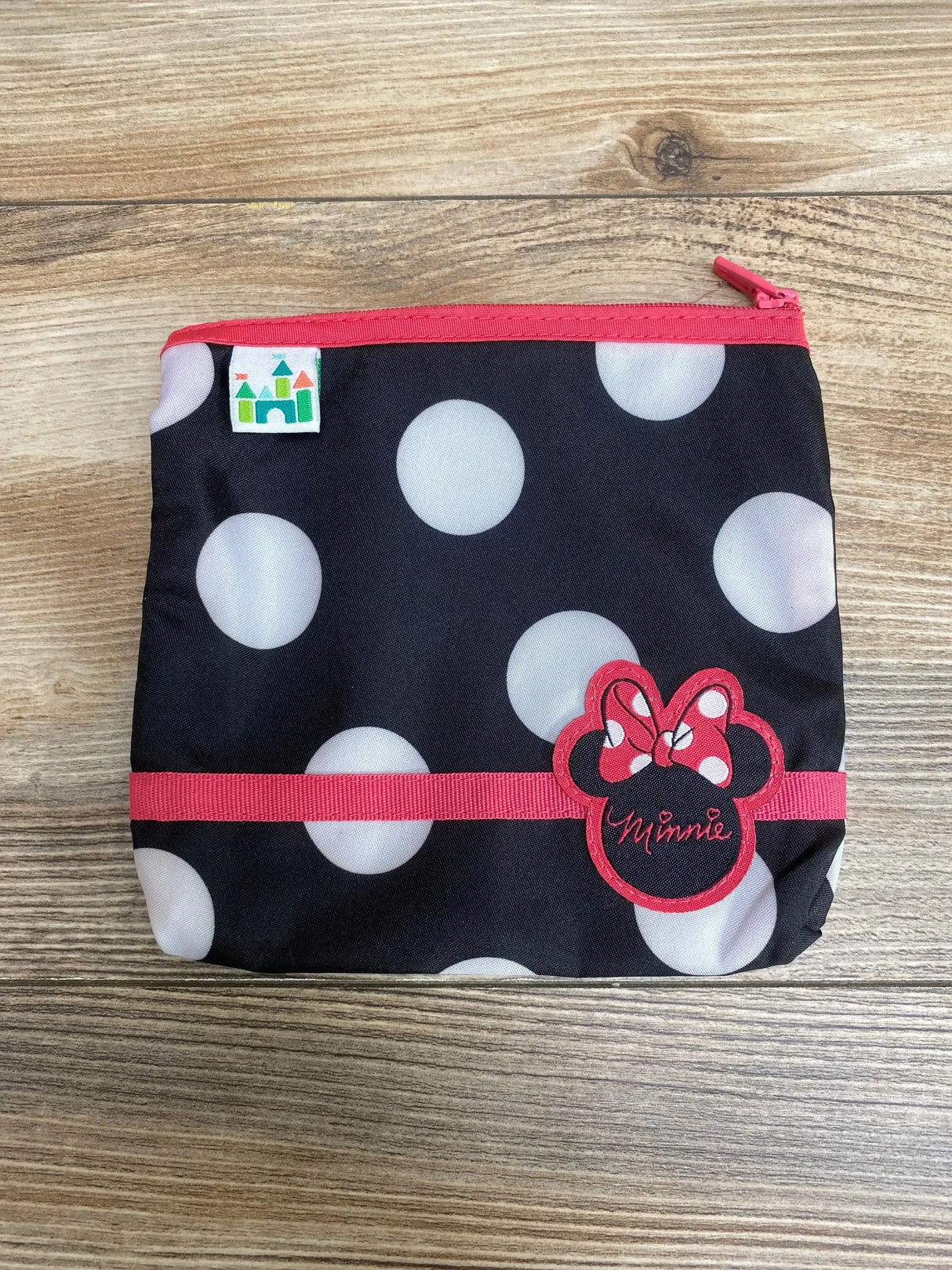 Front flat lay of Minnie Mouse zip carrying case, black polka dot fabric with red zipper and embroidered Minnie patch on wood