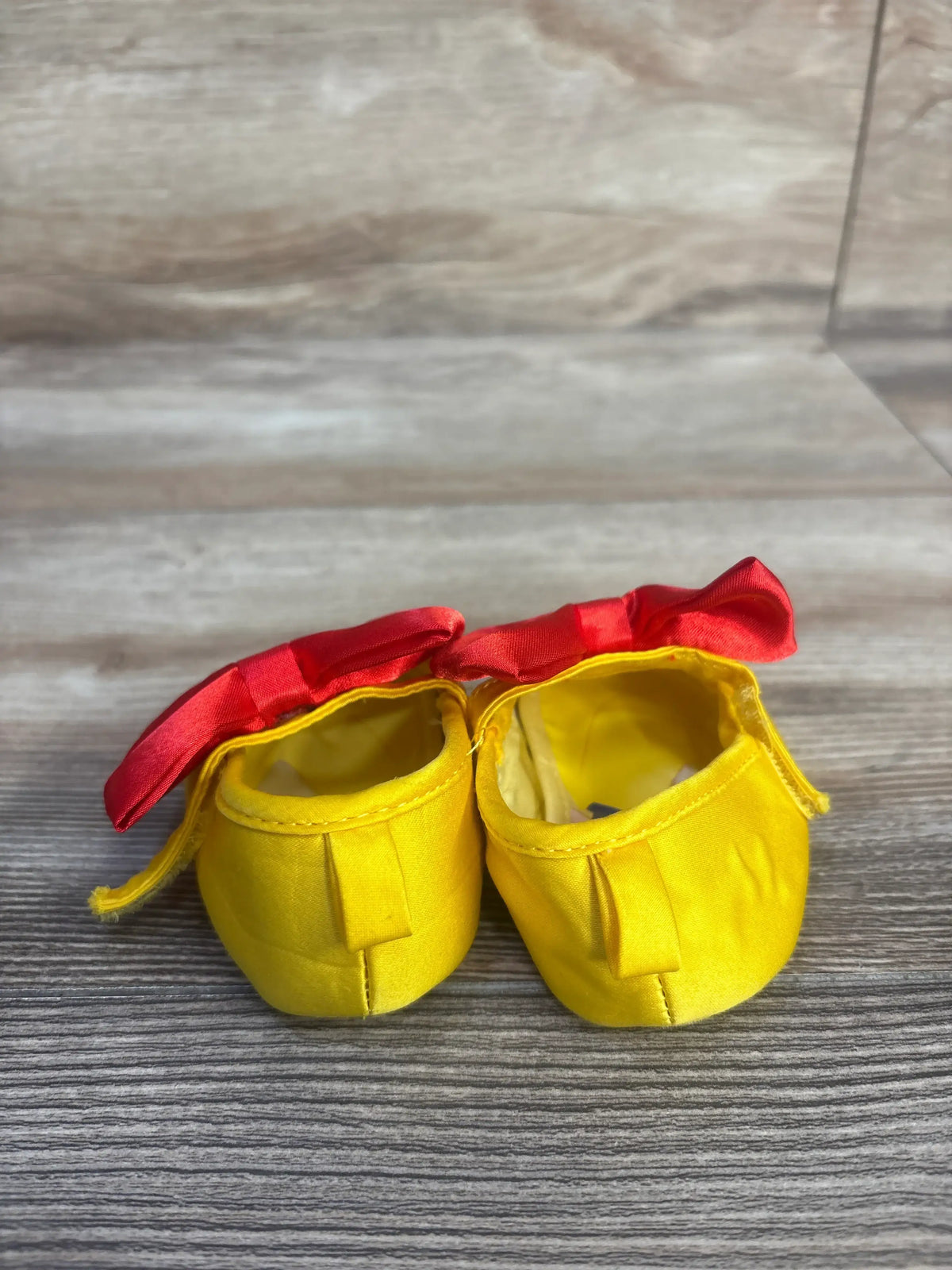Front view of Disney Baby Snow White soft sole shoes in yellow, showcasing red bows and pull tabs