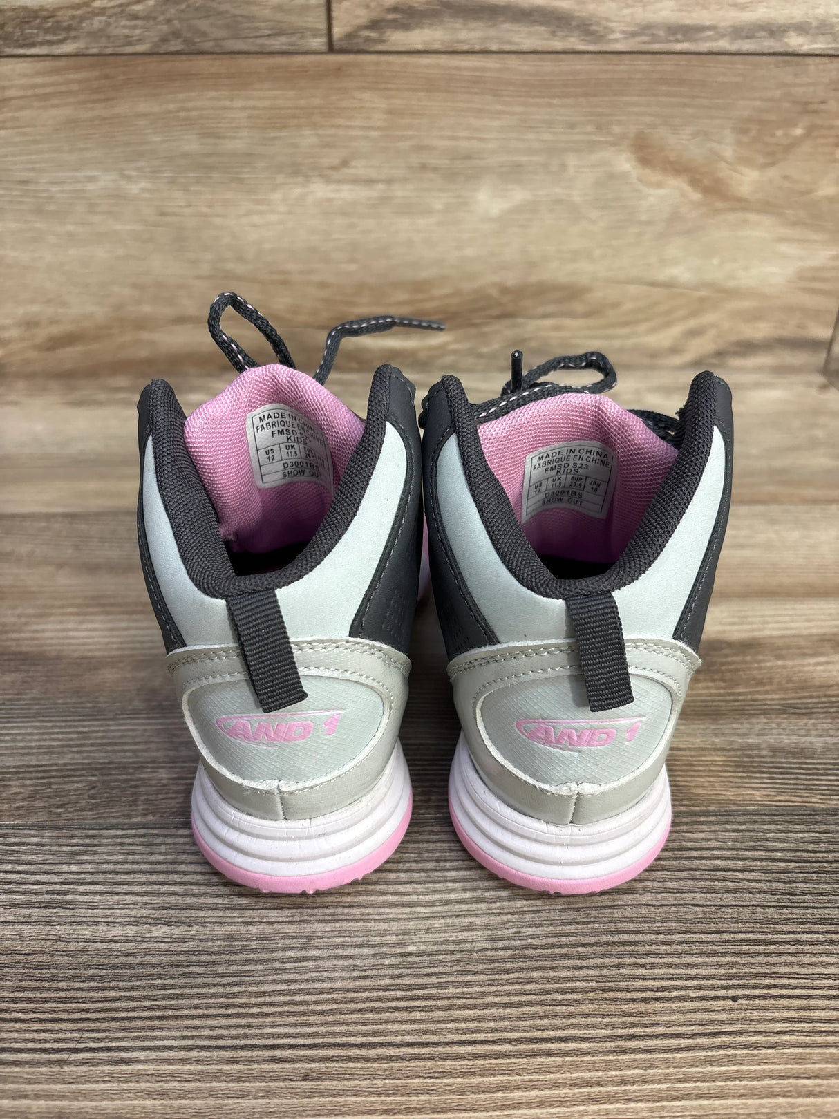 Pair of And1 kids basketball shoes in gray and pink on wooden floor, back view