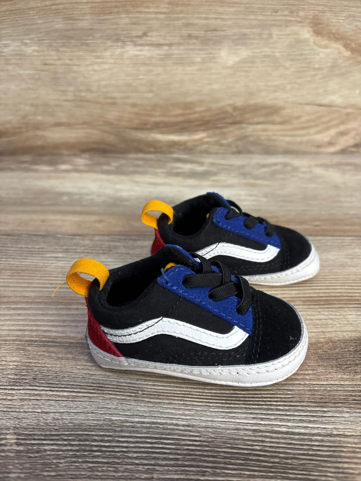 Front view of black Vans Old Skool crib shoes showcasing blue accents, white side stripes, red heels, and yellow pull tabs