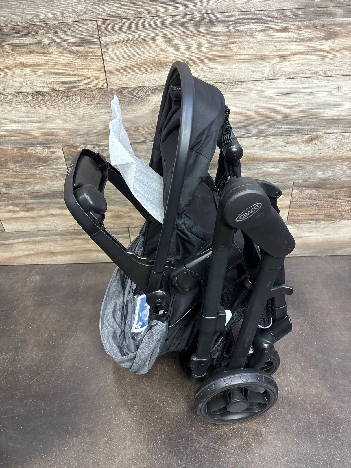 Folded black Graco stroller with foam padding, compact and ready for storage or transport