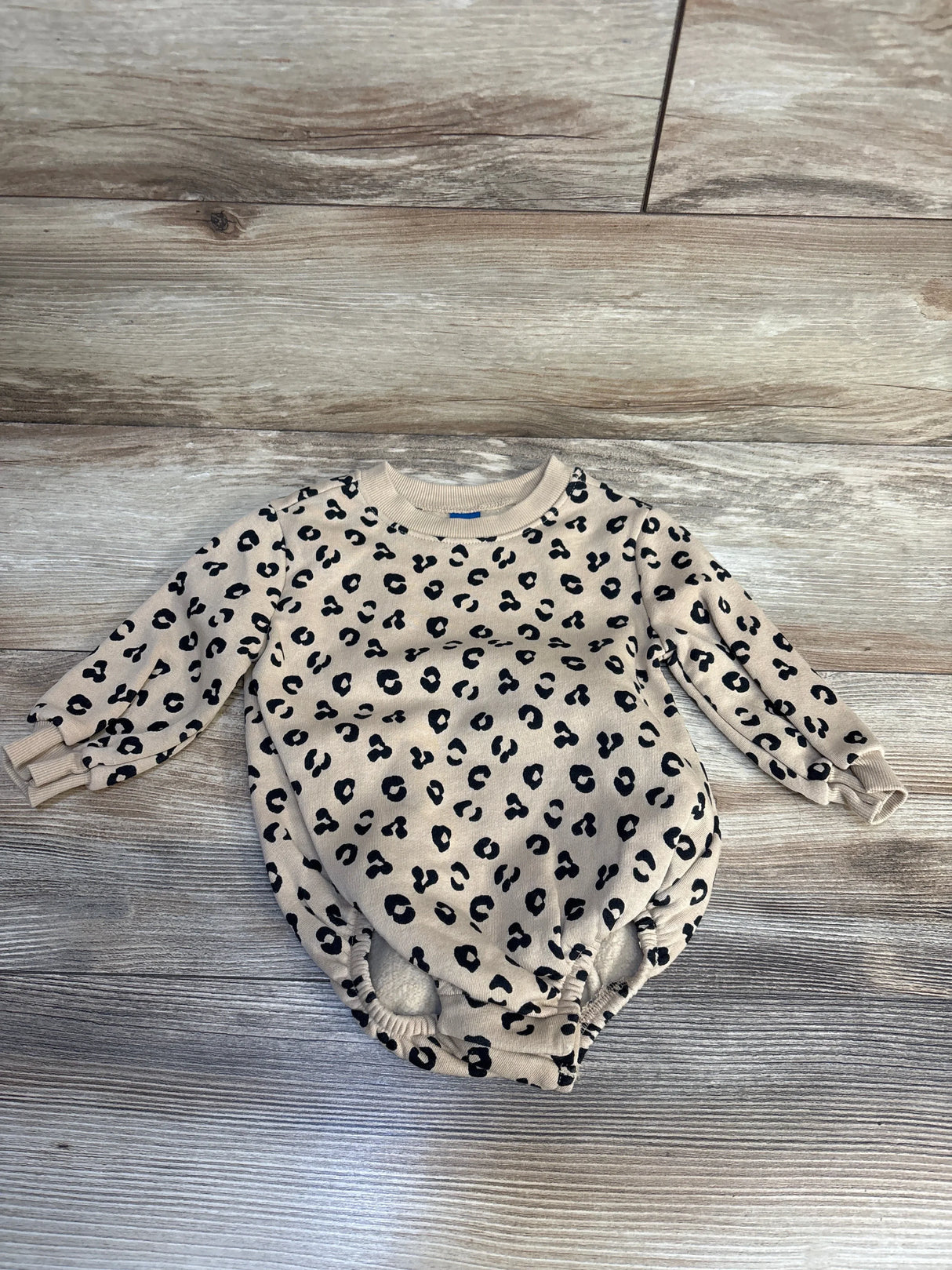Beige baby onesie with black leopard print, long sleeves, laid on wood floor