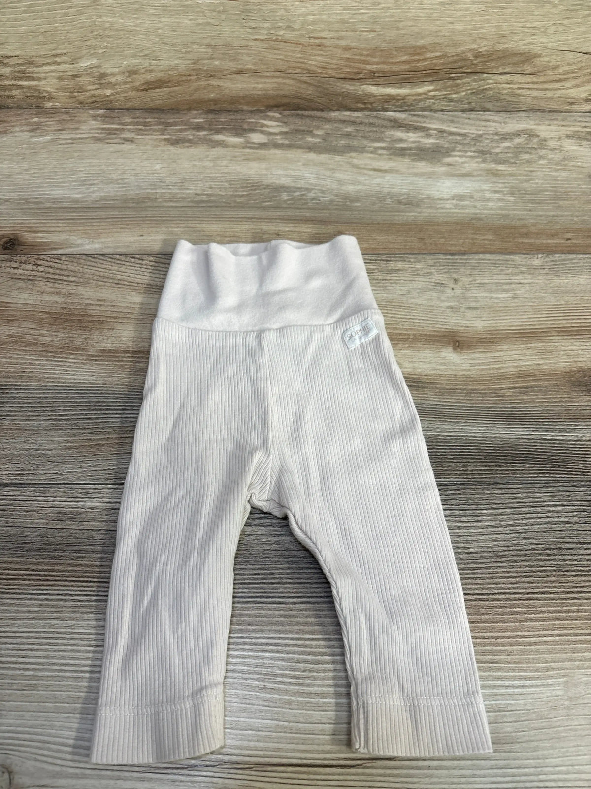 Flat lay of cream newborn ribbed pants with foldover waistband and ribbed texture on light wood background