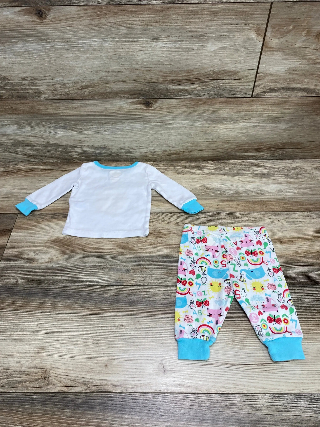 Flat lay of 2-piece pajama set: white long-sleeve top with turquoise trim and multicolor printed pants on wood floor