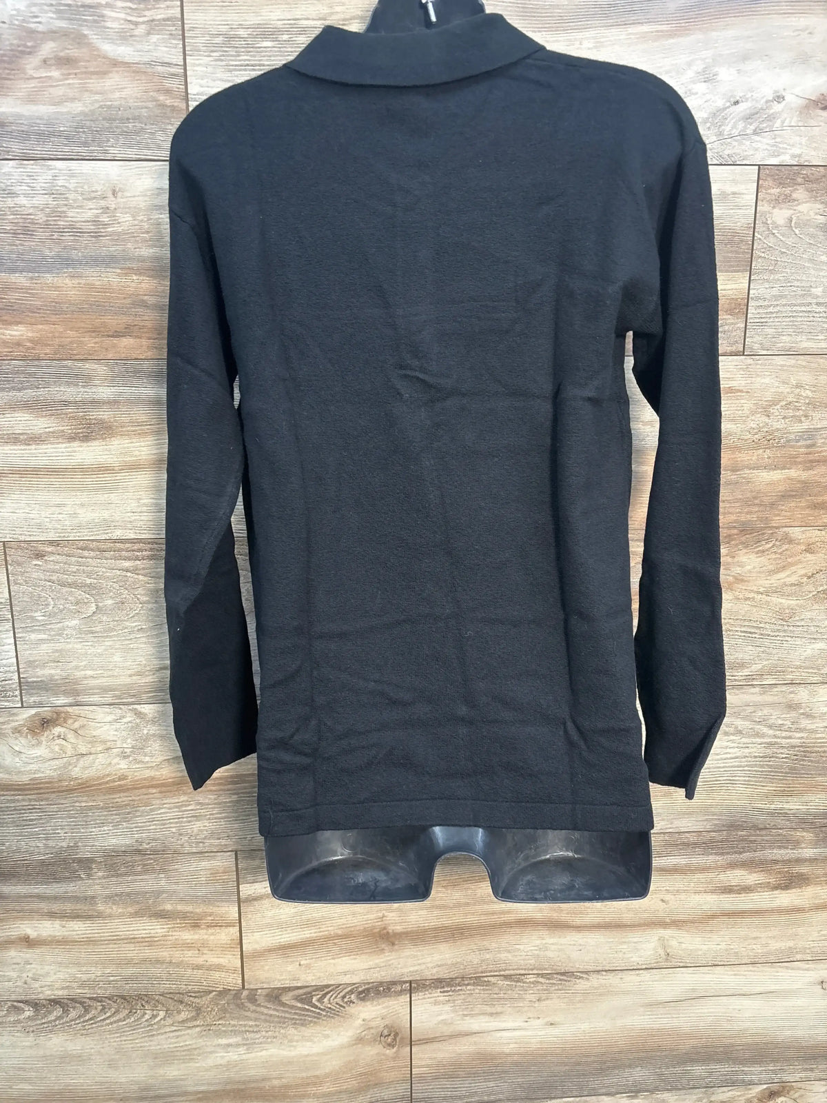 Back view of black maternity polo sweater showing collar, long sleeves, and straight hem on mannequin against wood background