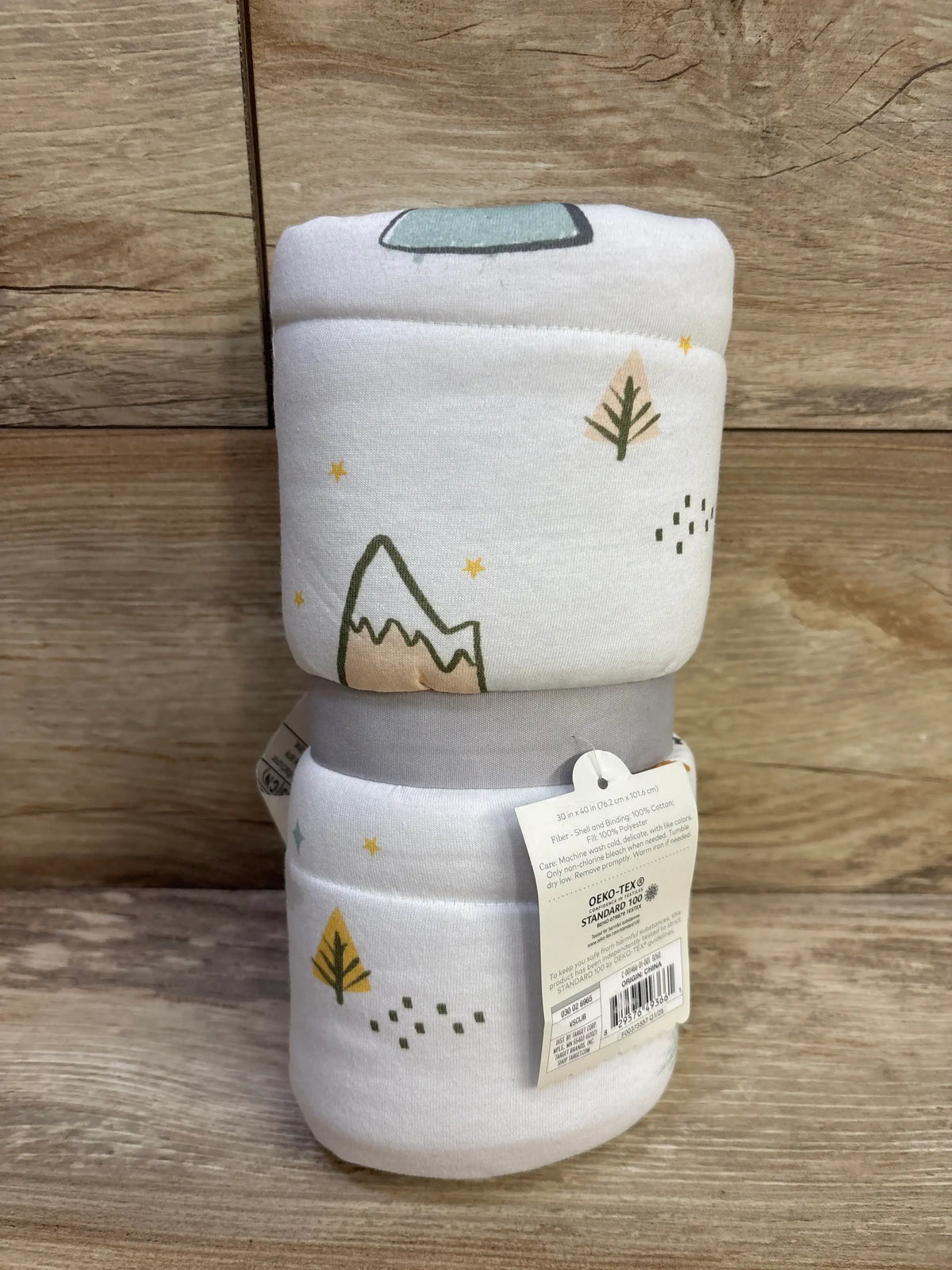 Front view of Cloud Island reversible jersey-knit baby blanket rolled and stacked showing mountain and tree print on wood background