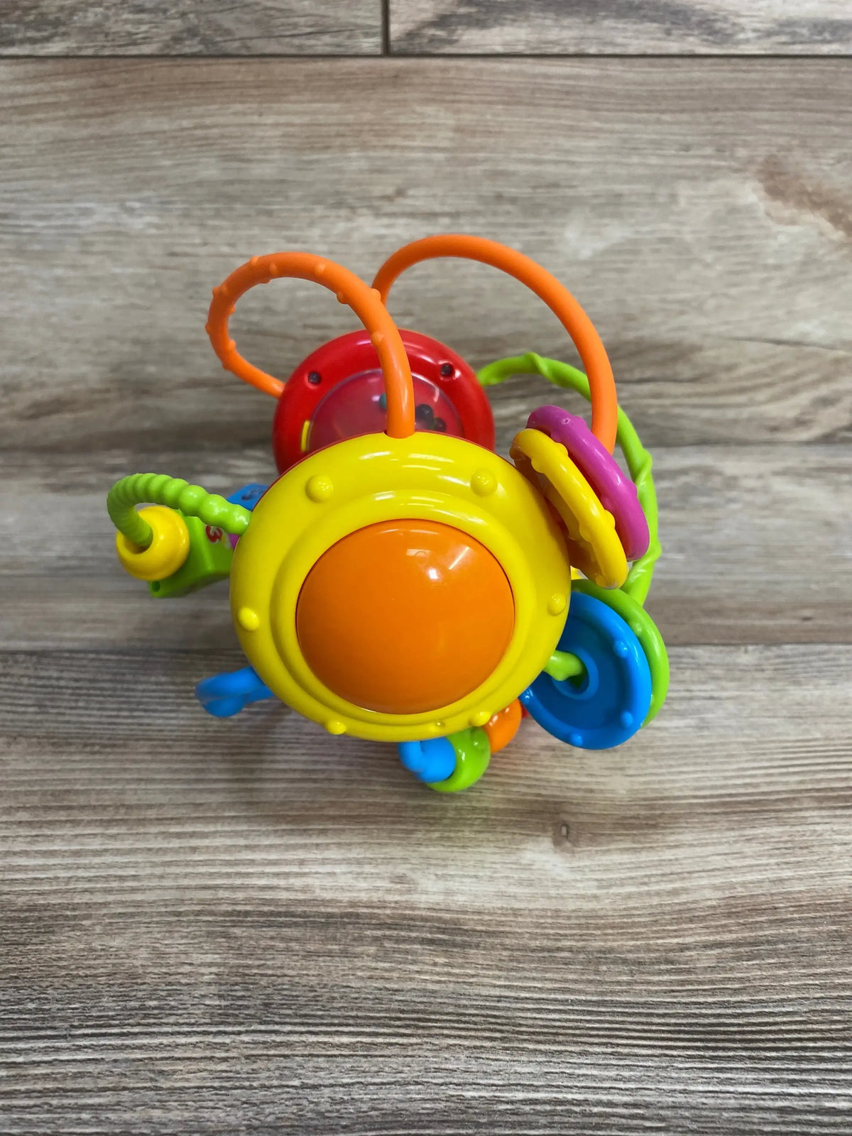 Front view of Grab N Shake activity ball with yellow orange rattle, textured loops and colorful rings on wood background
