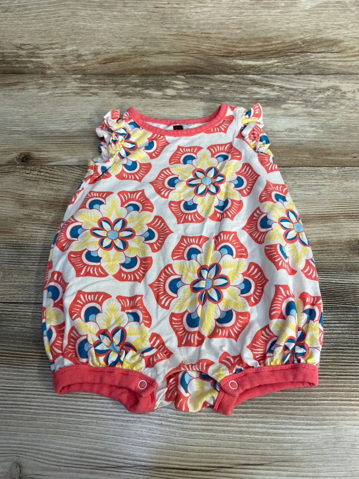 Top view of baby romper with coral trim and ruffled sleeves, white fabric with floral print, snap crotch on wood background