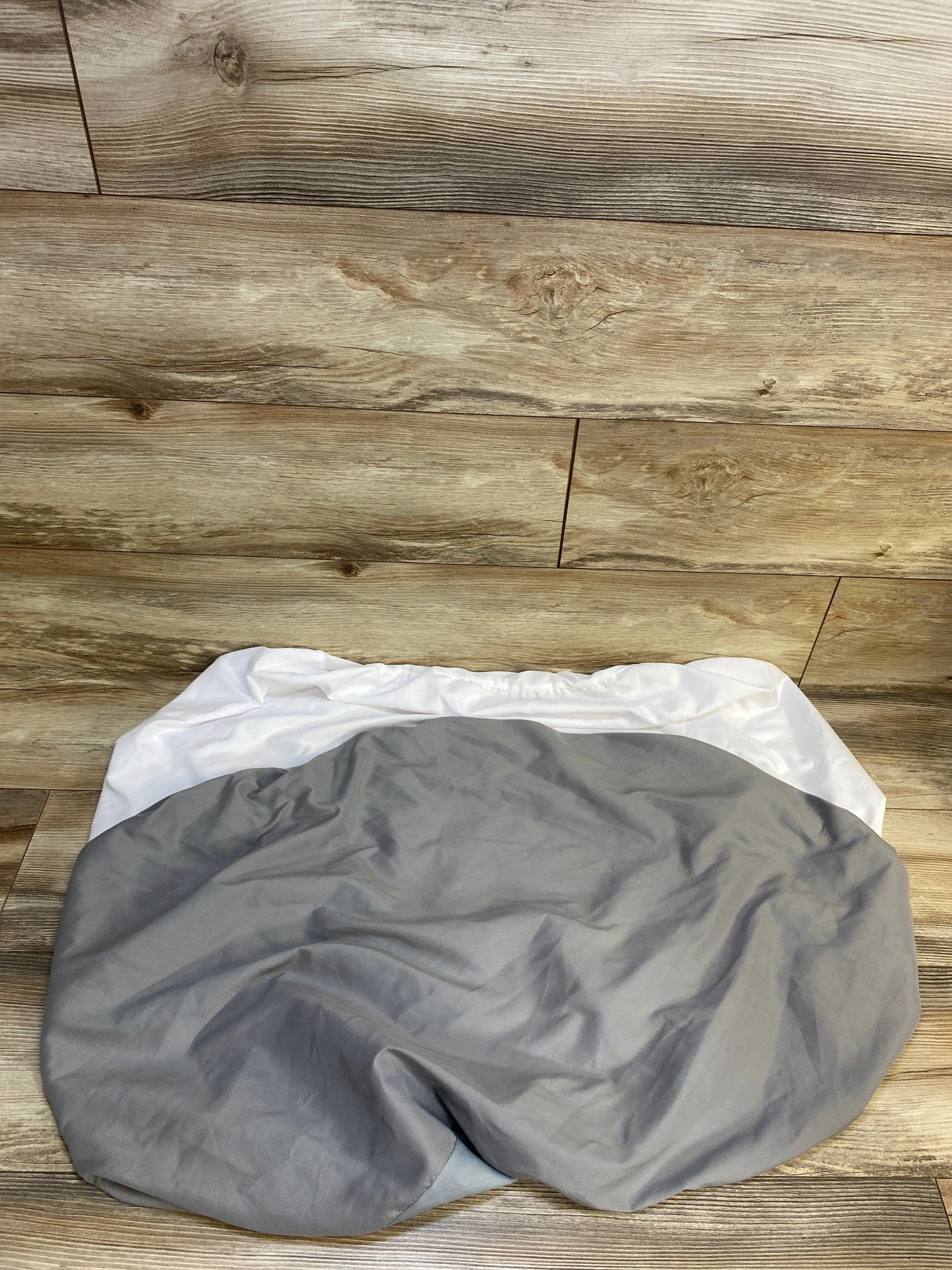 Top view of Biloban pack n play mattress protector in grey and white showcasing fitted elastic skirt and waterproof fabric on wooden floor