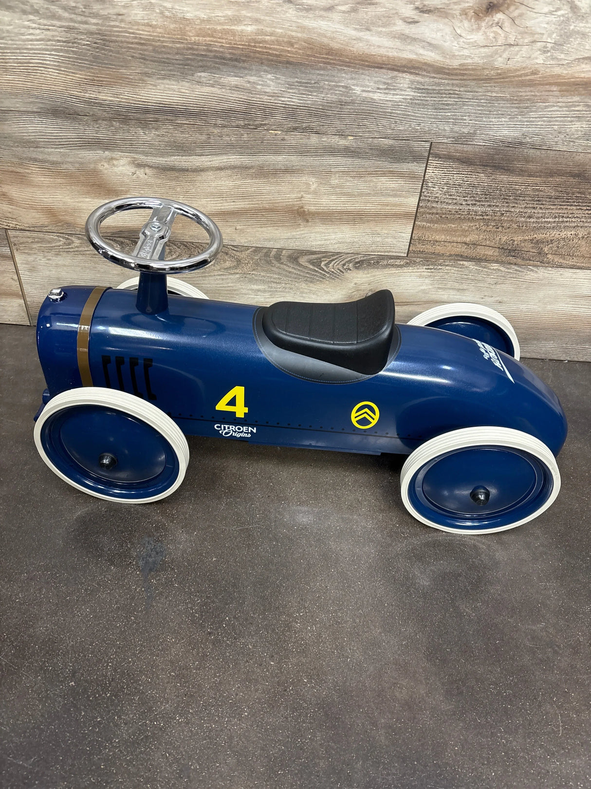 Blue vintage-style children's ride-on toy car with white tires, black seat, and silver steering wheel