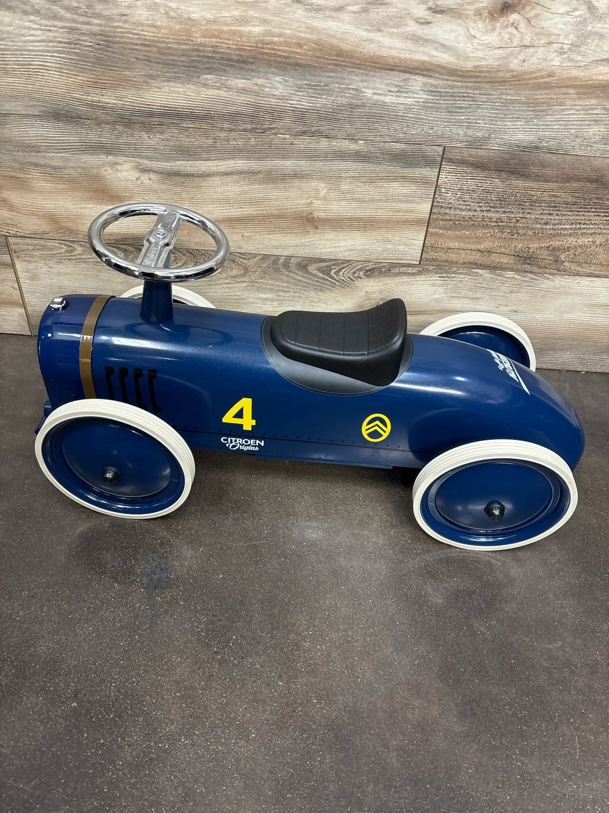 Blue vintage-style children's ride-on toy car with white tires, black seat, and silver steering wheel