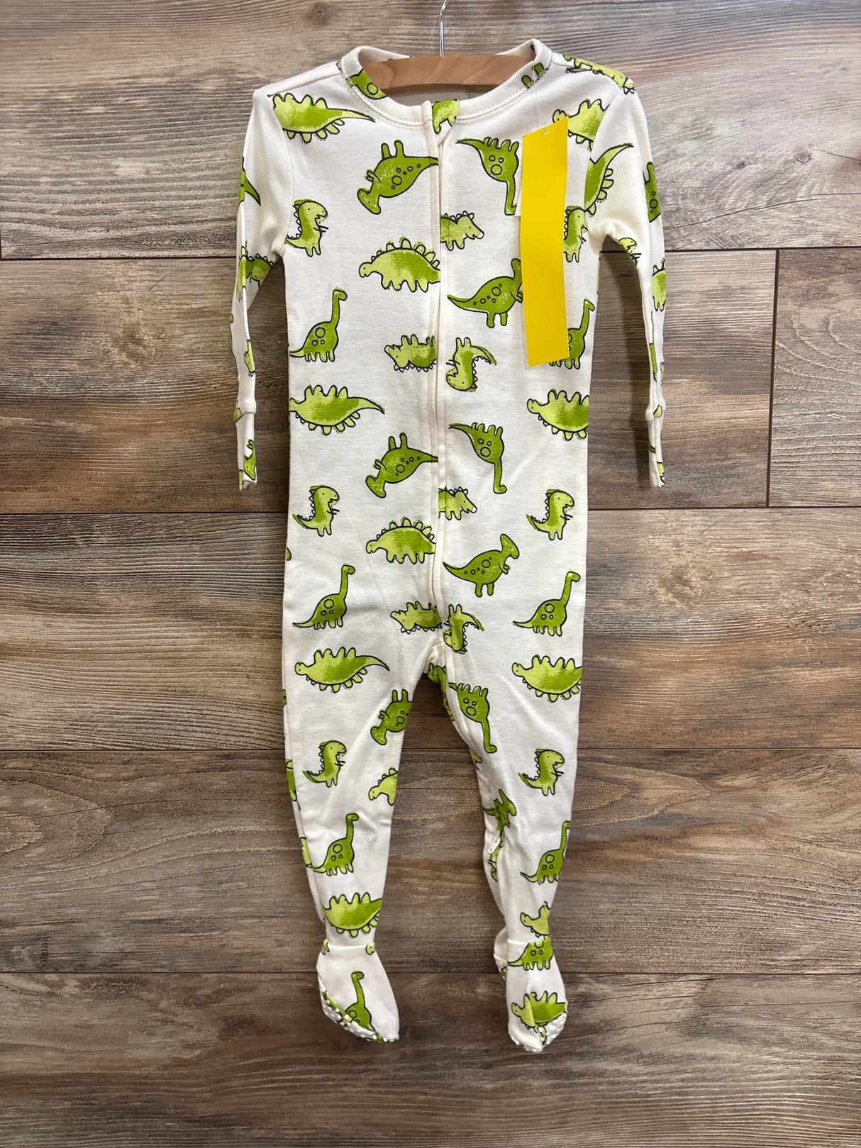 Front view of Old Navy white footed sleeper size 12-18 months showcasing all-over green dinosaur print and center zipper with wood plank background
