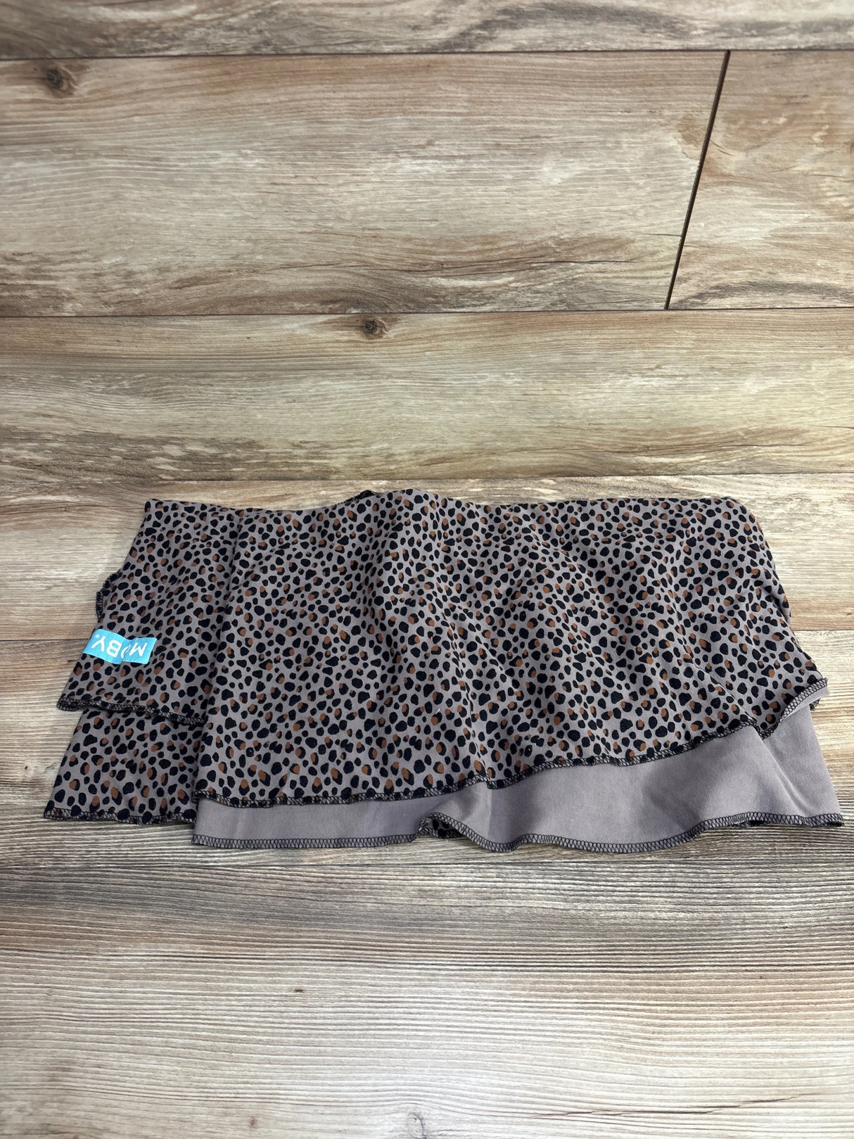 Folded view of Moby Classic Wrap baby carrier showcasing ruffled layers, cheetah print and blue MOBY tag on wood floor
