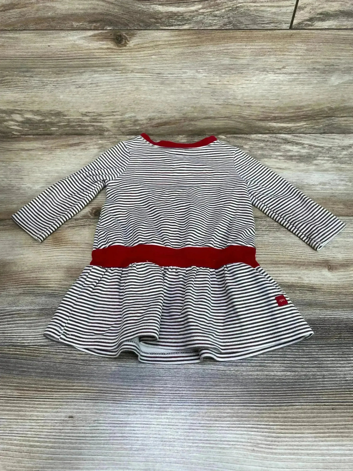 Flat lay of TEA striped twirl dress size 6 to 12 months showing black and white stripes with red neckline and waist band on wood floor