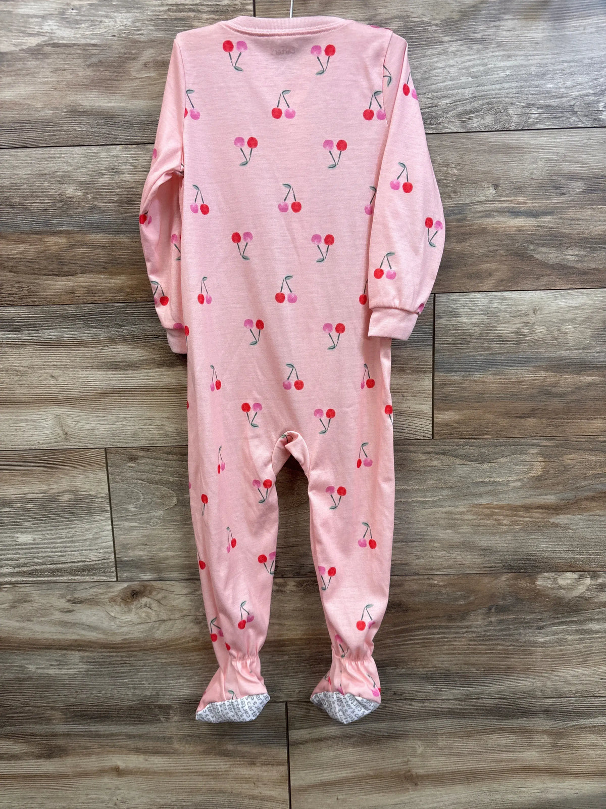 Front view of pink cherry-print sleeper with long sleeves and covered feet on a wood-look floor
