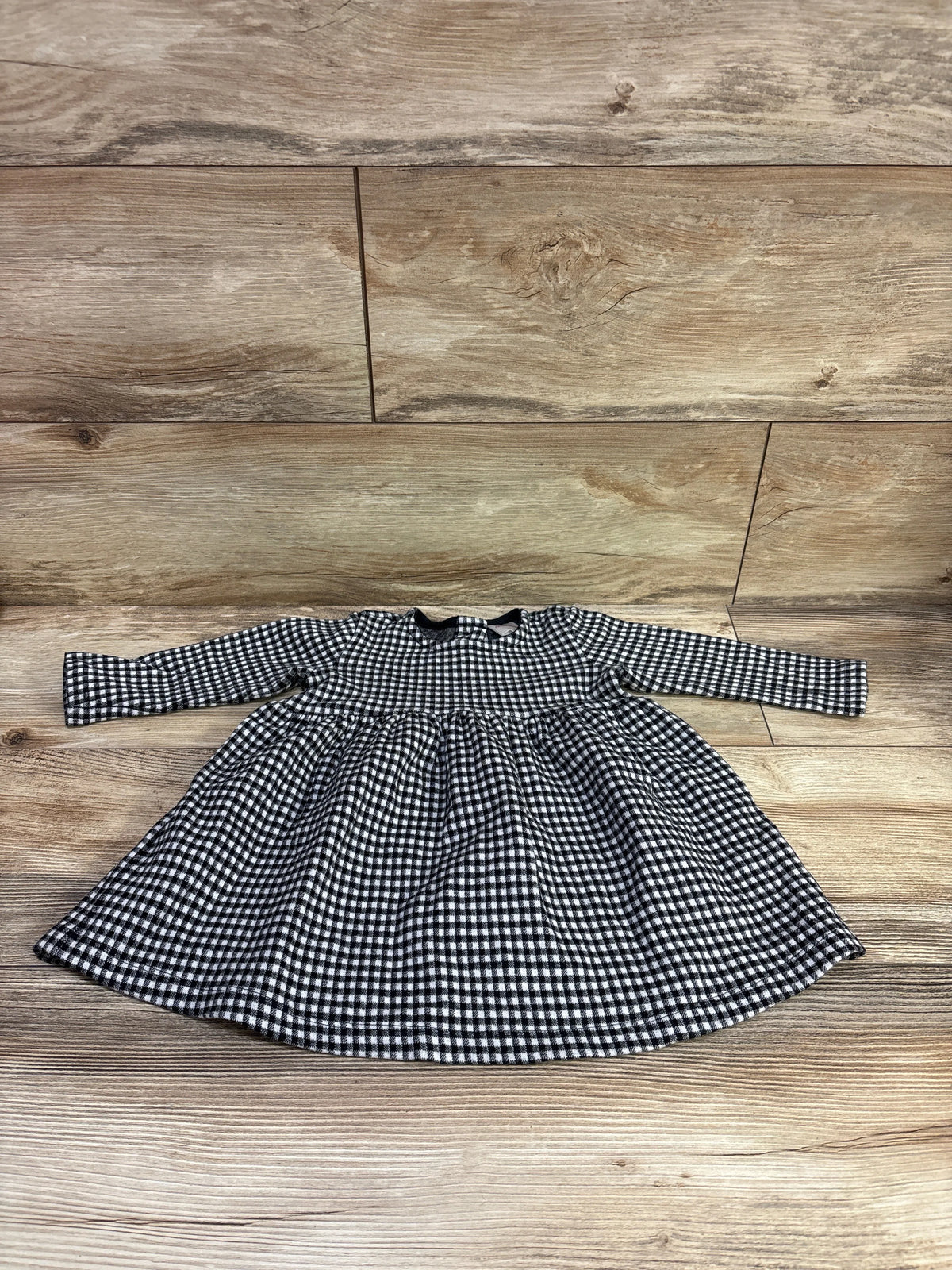 Front view of Hanna Andersson long sleeve gingham dress in size 12 to 18 months showcasing gathered waist and flared skirt on a wood floor