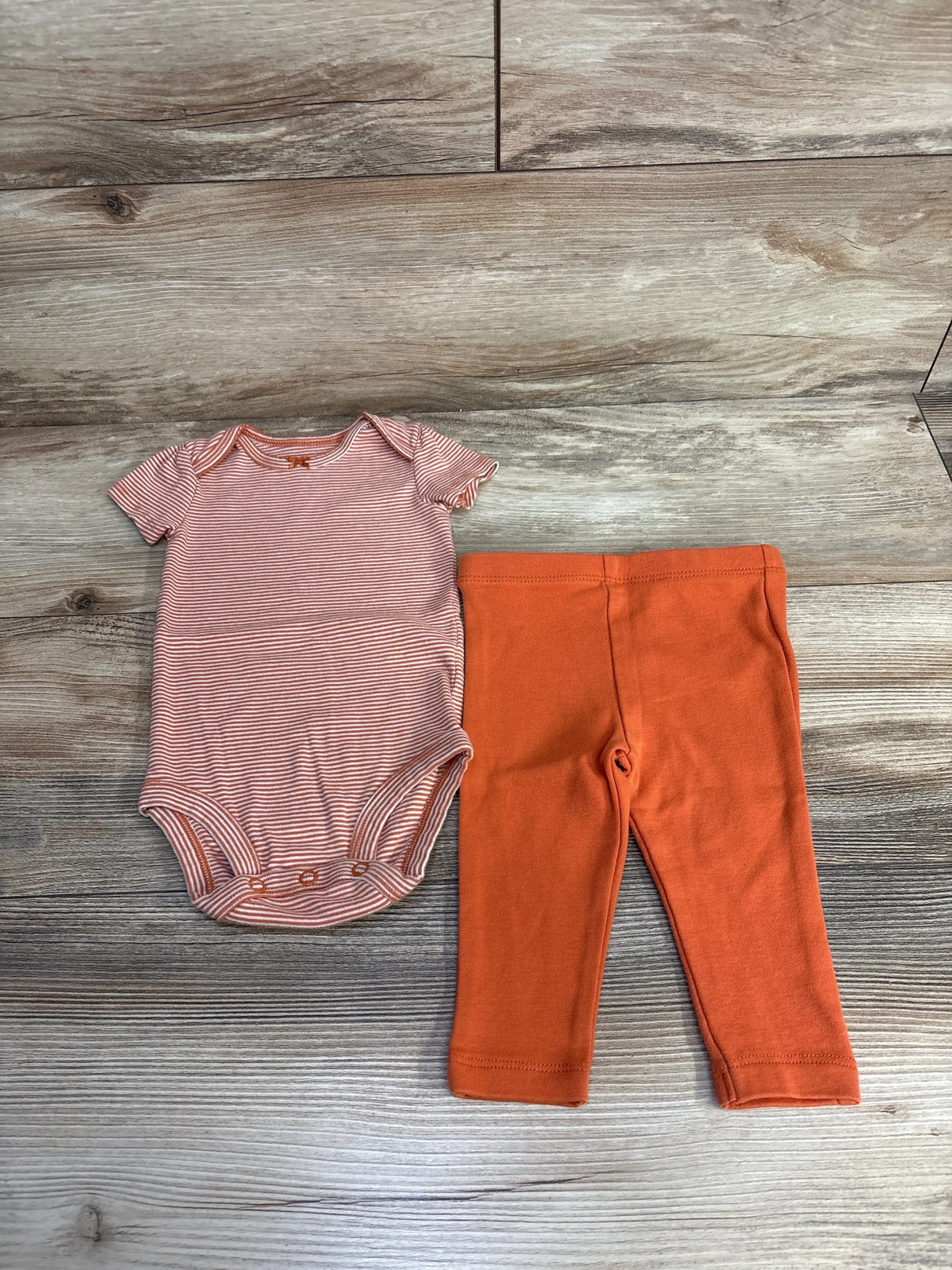 Striped peach baby bodysuit and solid orange leggings on wood background