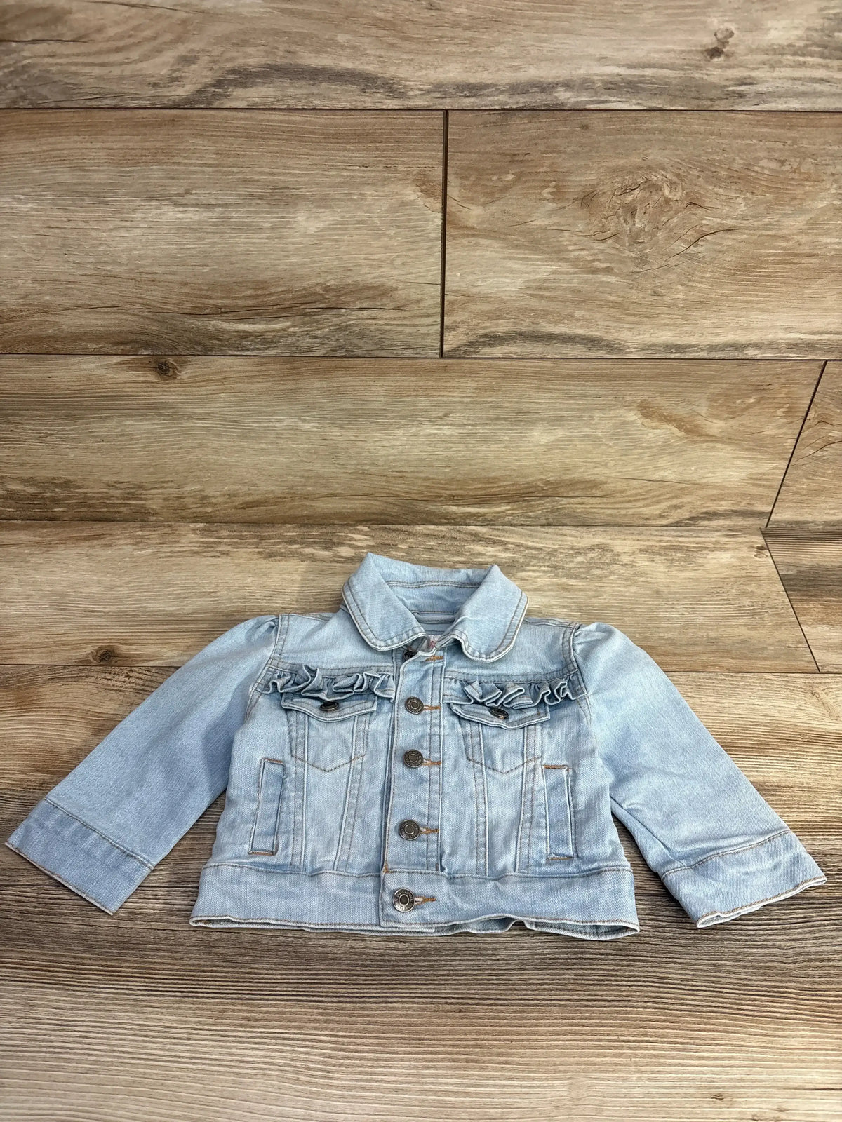 Light blue toddler denim jacket with ruffled chest pockets on wood background