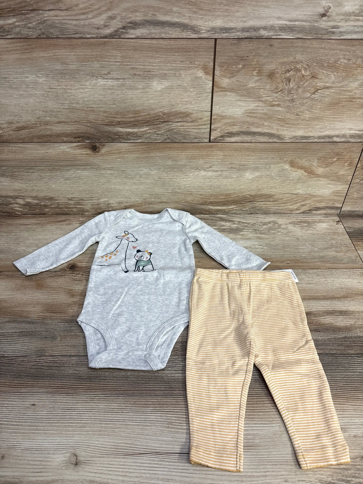 Gray long sleeve baby bodysuit with giraffe print and beige striped baby leggings on wood floor