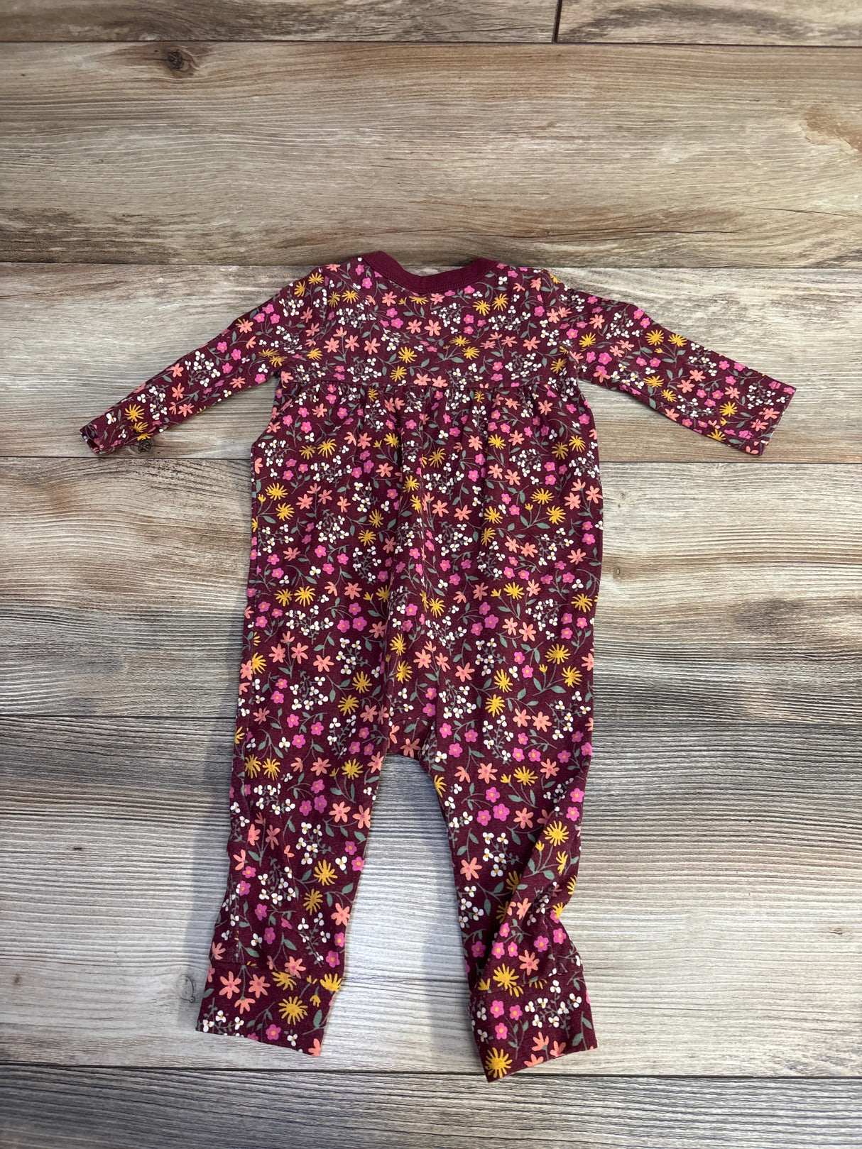 Floral baby romper with pink, yellow, and white flowers on wood floor