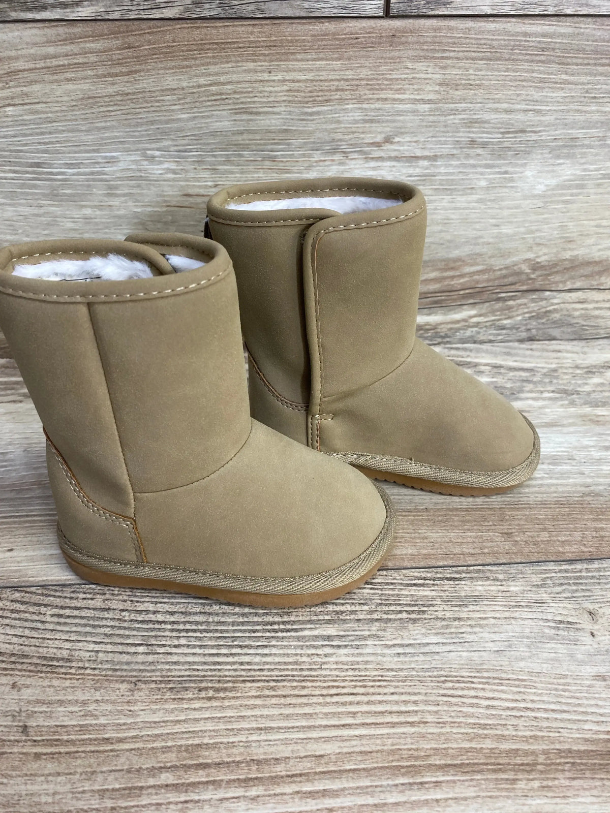 Tan toddler boots with plush lining on wooden background, kids winter footwear