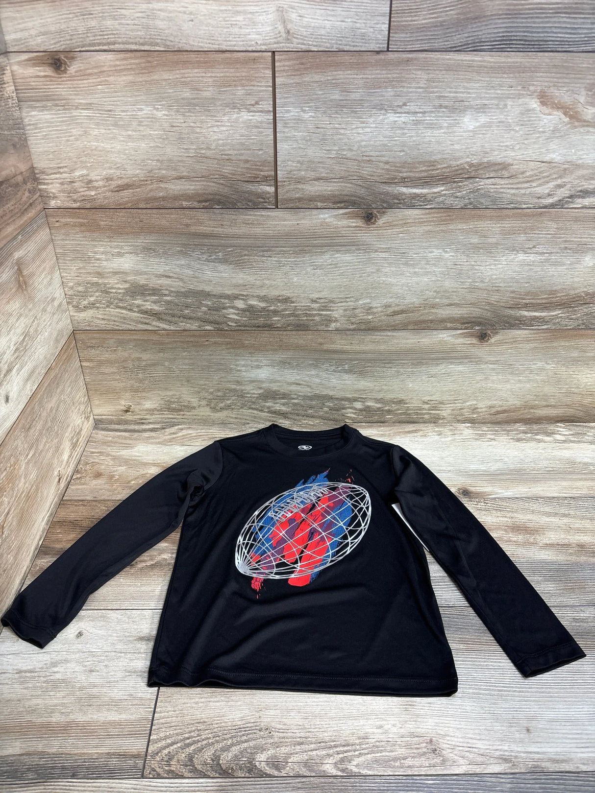 Black long sleeve kids shirt with red and blue abstract globe graphic on wood floor
