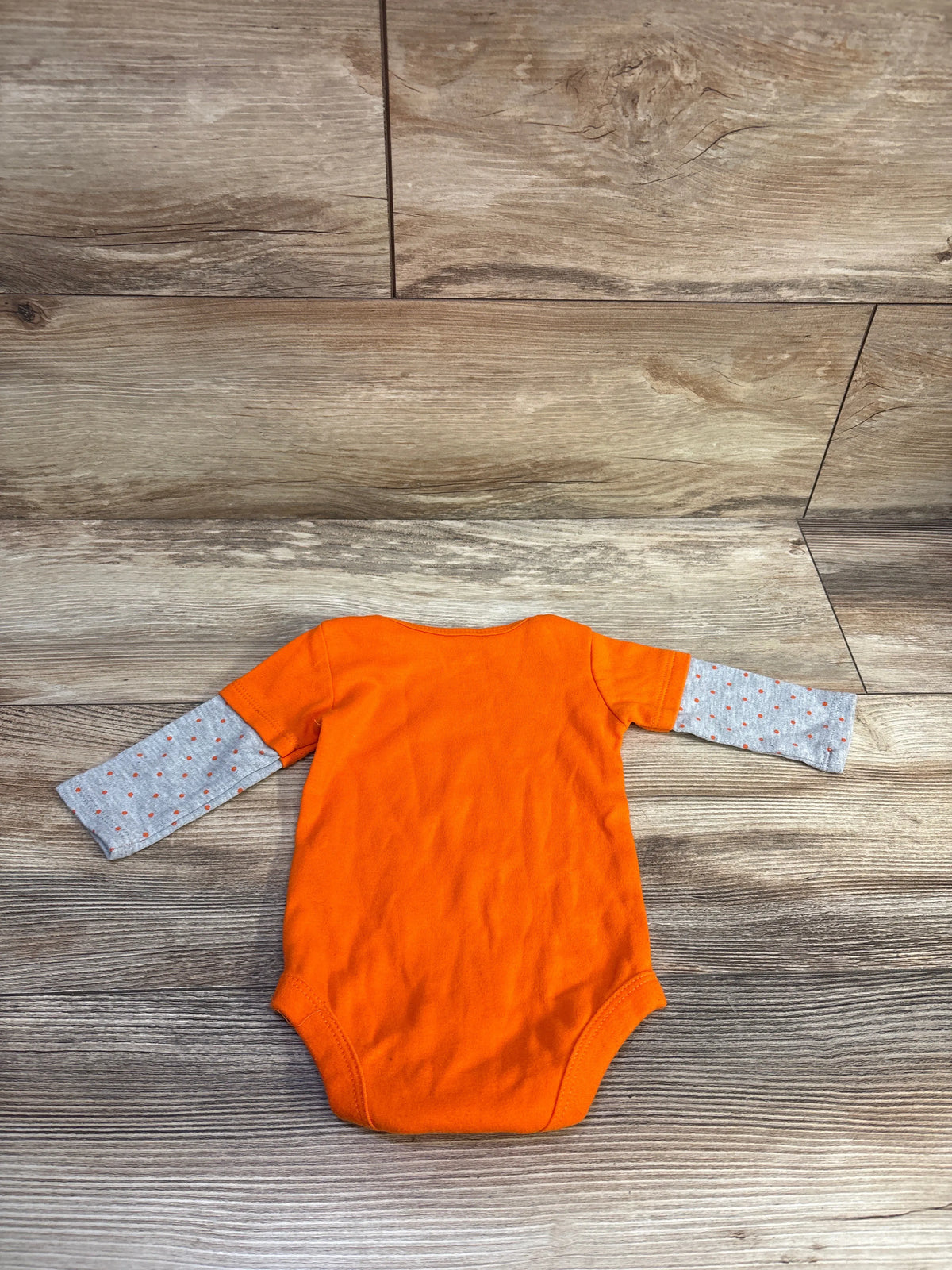 Front view of orange Halloween bodysuit in size 0-3 months showcasing gray sleeves with orange dots on a wood floor