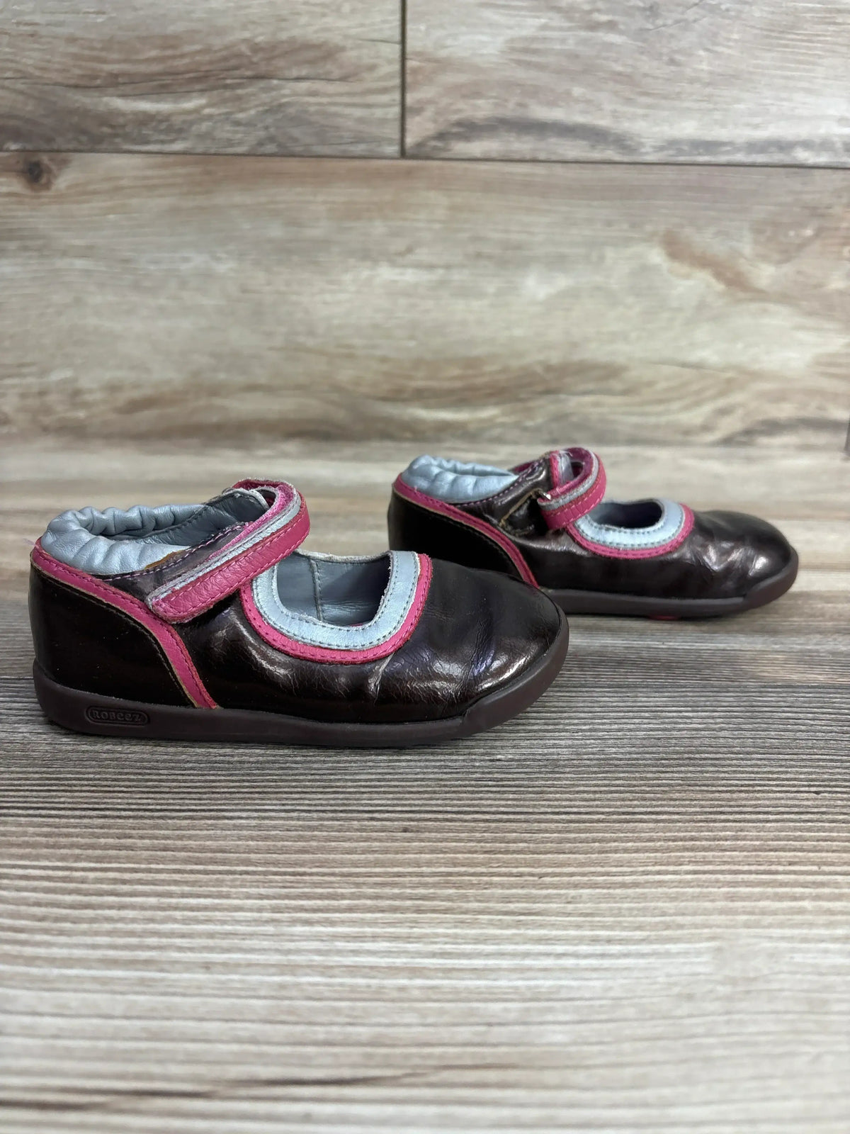 Pair of brown toddler shoes with pink and gray accents and velcro straps on wooden surface
