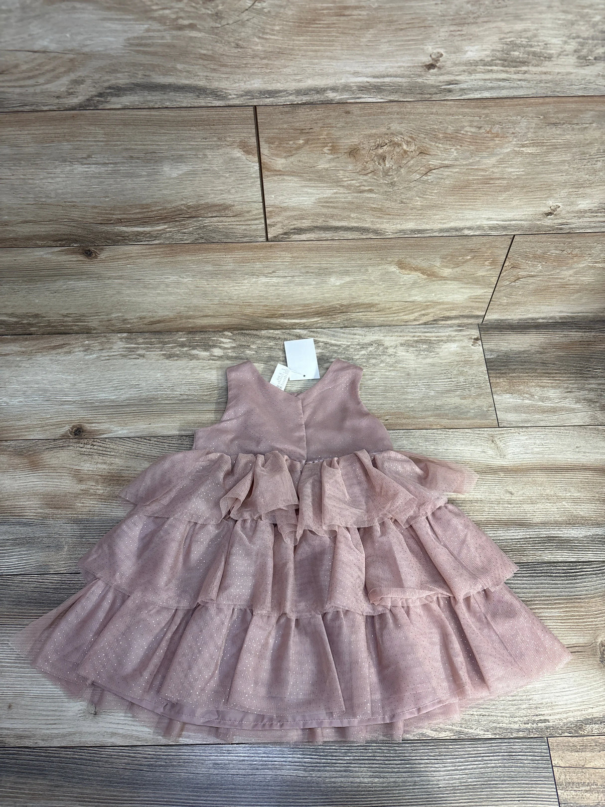 Pink sleeveless toddler dress with tiered ruffles and sparkly fabric on wooden floor