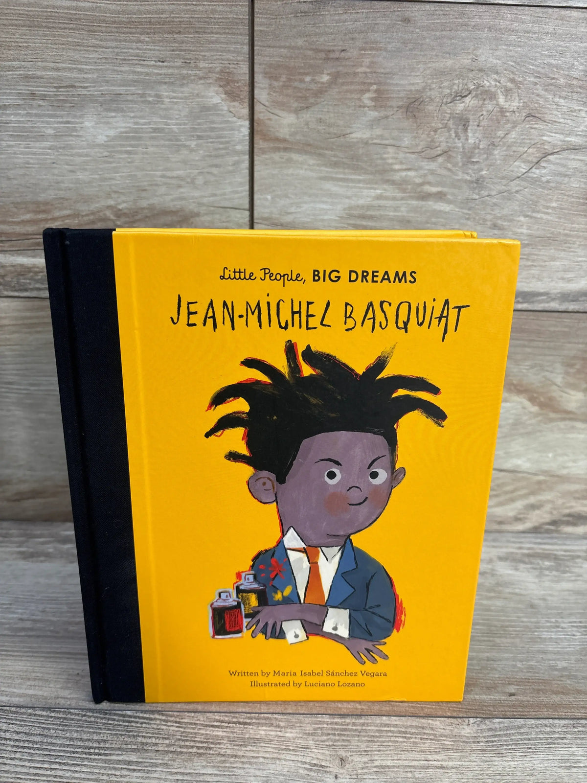 Front view of Jean-Michel Basquiat hardcover book showcasing yellow illustrated cover and black spine on a wood surface
