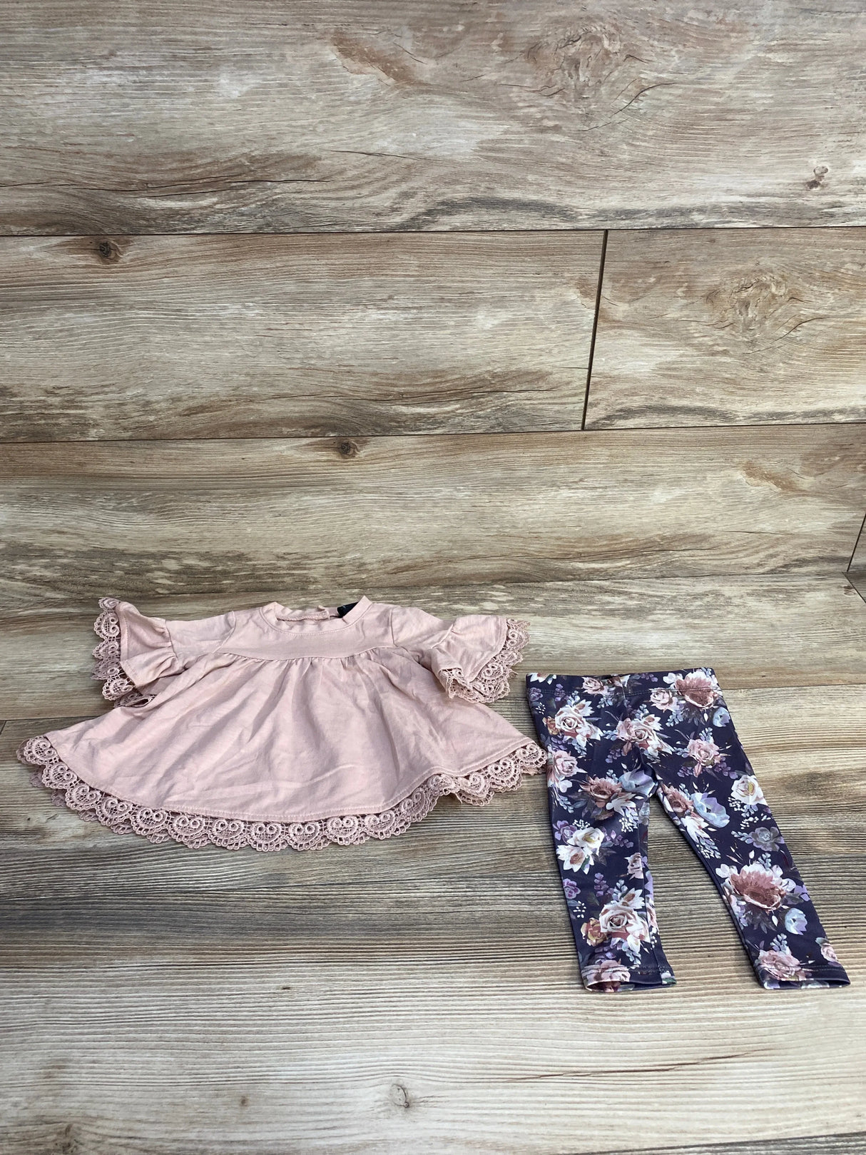 Flat lay of Cynthia Rowley 2-piece baby top and leggings showcasing pink lace-trim swing top and navy floral leggings on light wood background