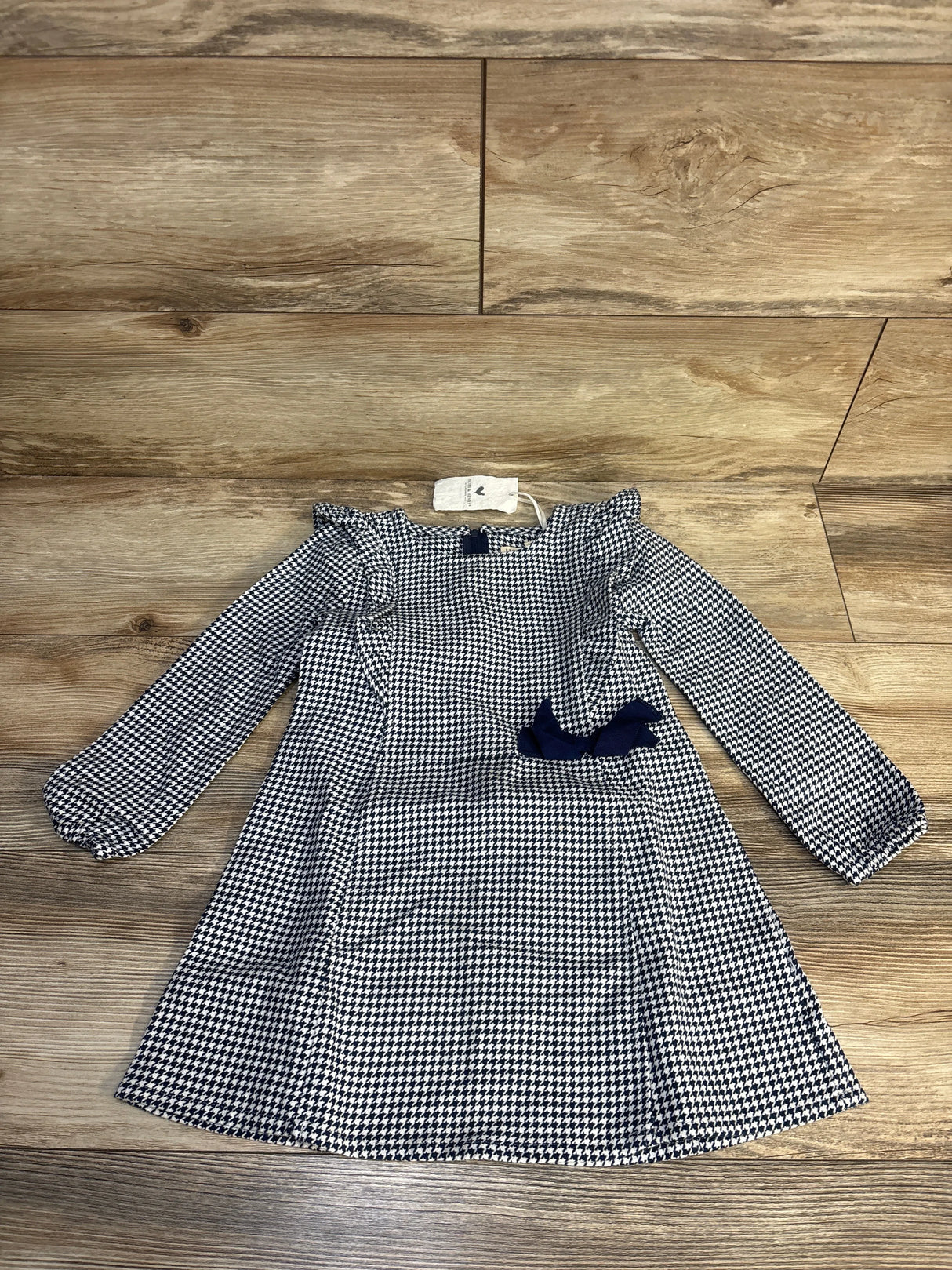 Girls' houndstooth long sleeve dress with navy bow, laid flat on wood floor.