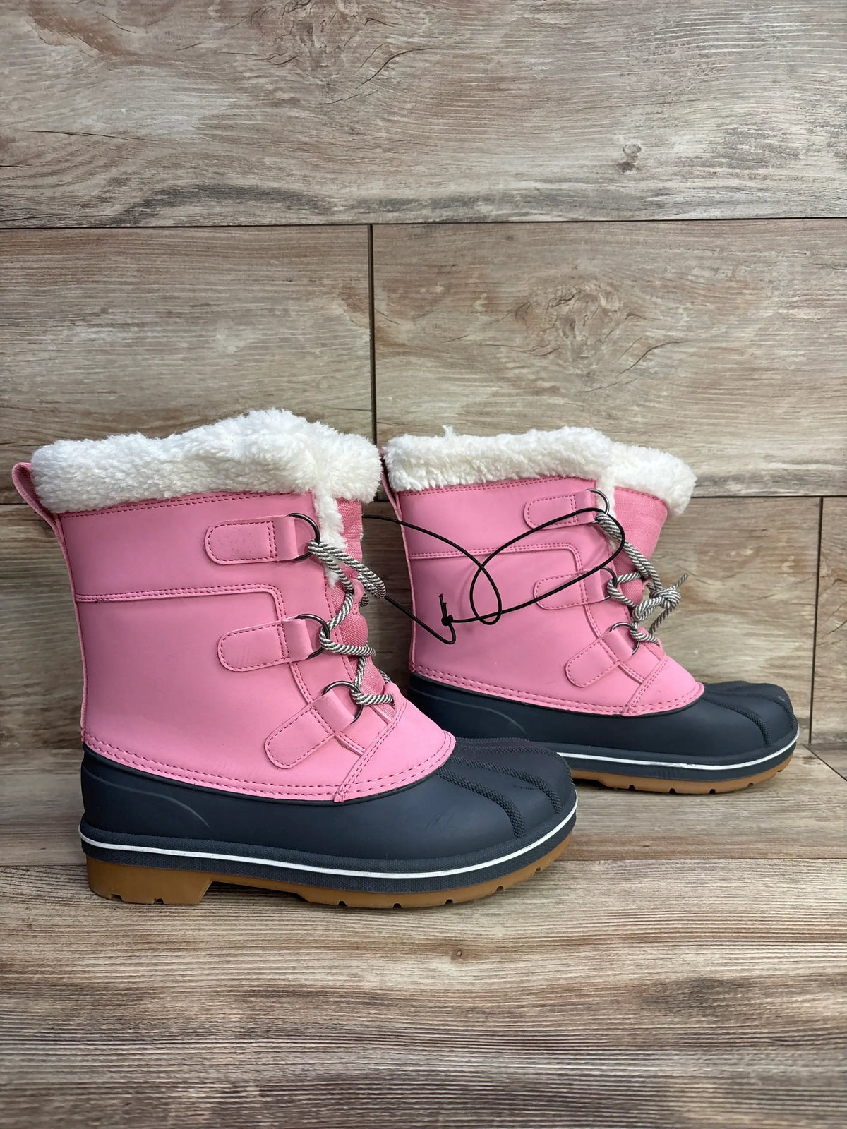 Pink kids winter snow boots with faux fur lining and rubber soles on wooden background