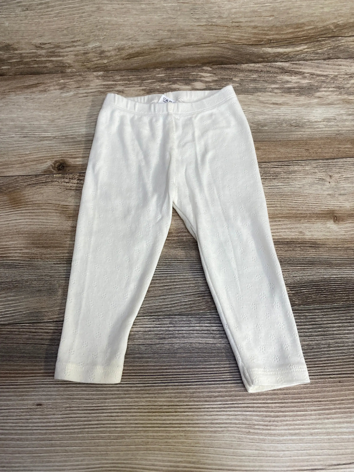 Flat lay of Viverano organic pointelle baby leggings, white, 3 to 6 months, showing knit texture on light wood background