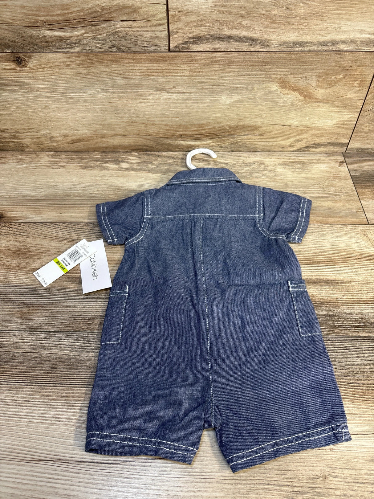 Denim short sleeve baby romper with pockets and hanger, laid on wooden floor