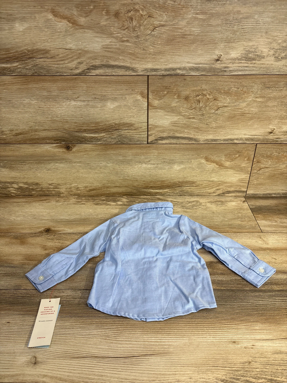 Light blue long sleeve baby shirt with tag on wood floor background