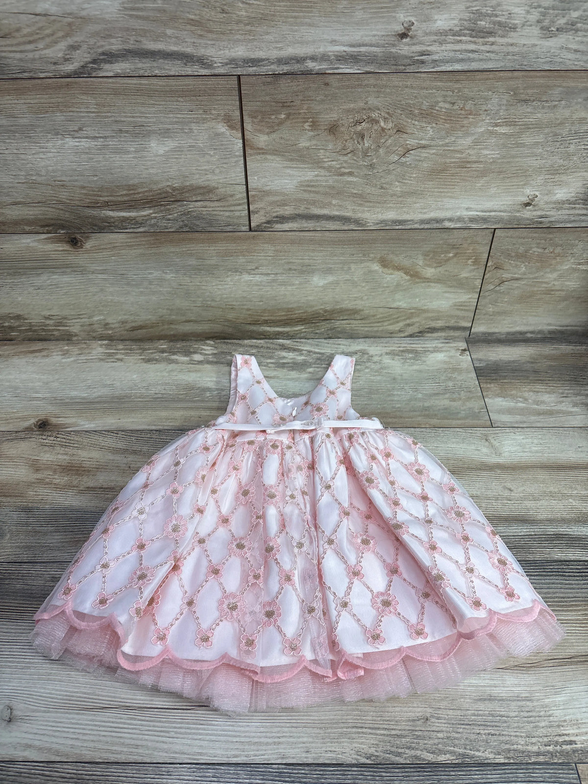 Pink couture princess dress with golden floral accents and tulle hem on wood background