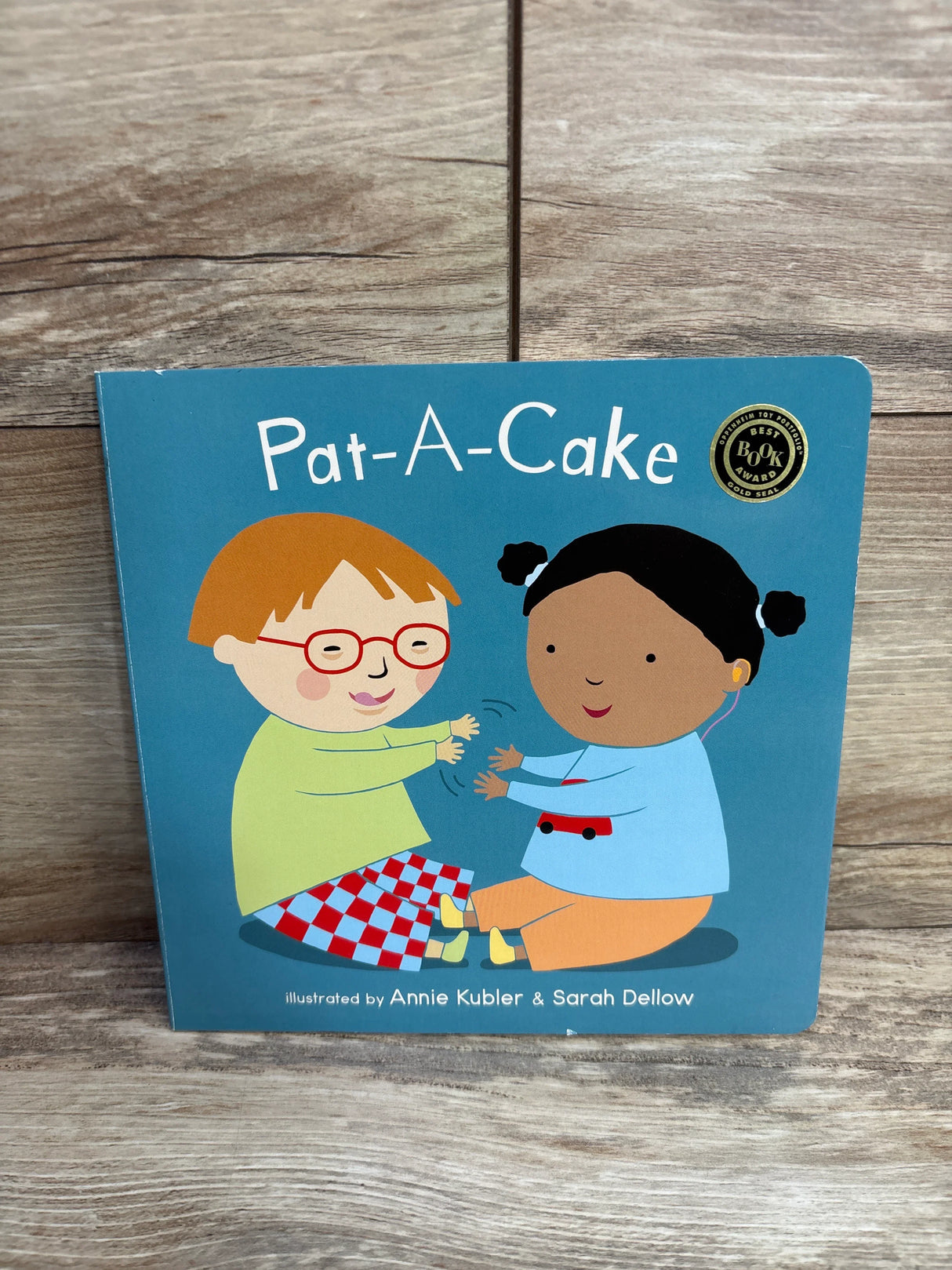 Pat-A-Cake board book cover with two children playing, wooden background