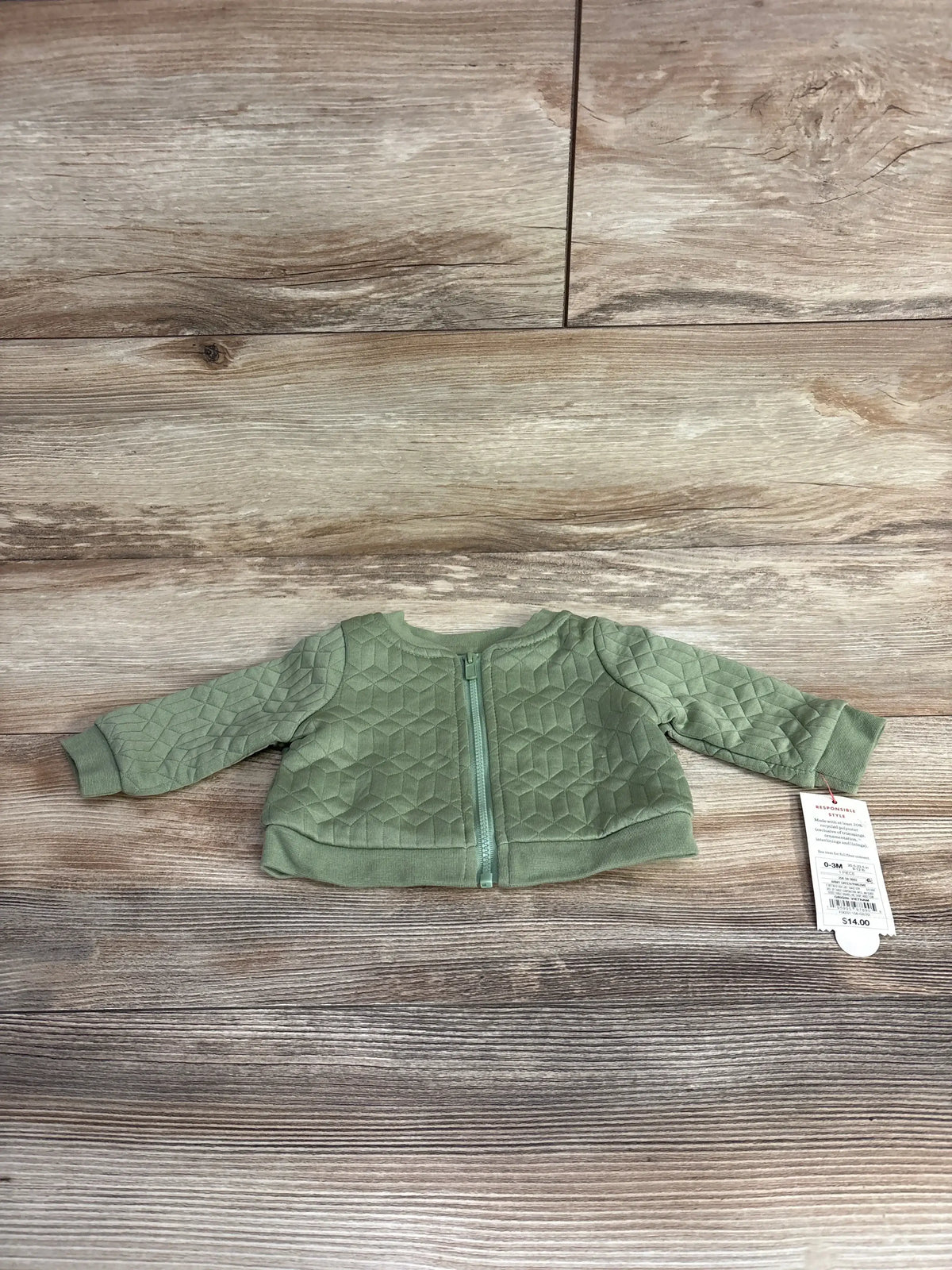 Green quilted baby jacket with zipper and price tag on wooden floor