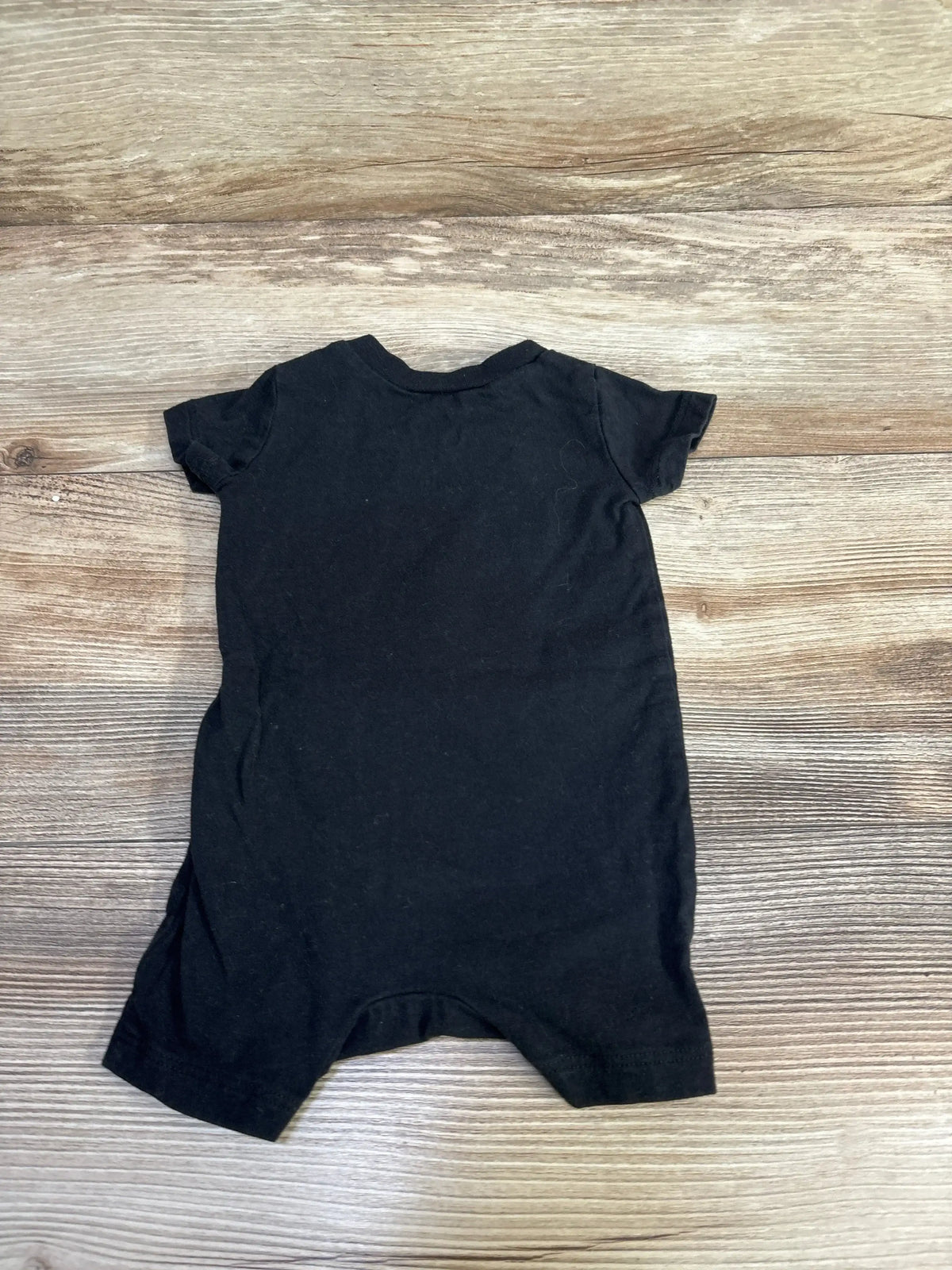 Flat lay of back of black Nike shortie romper size 3M showing short sleeves and crew neckline on wood floor