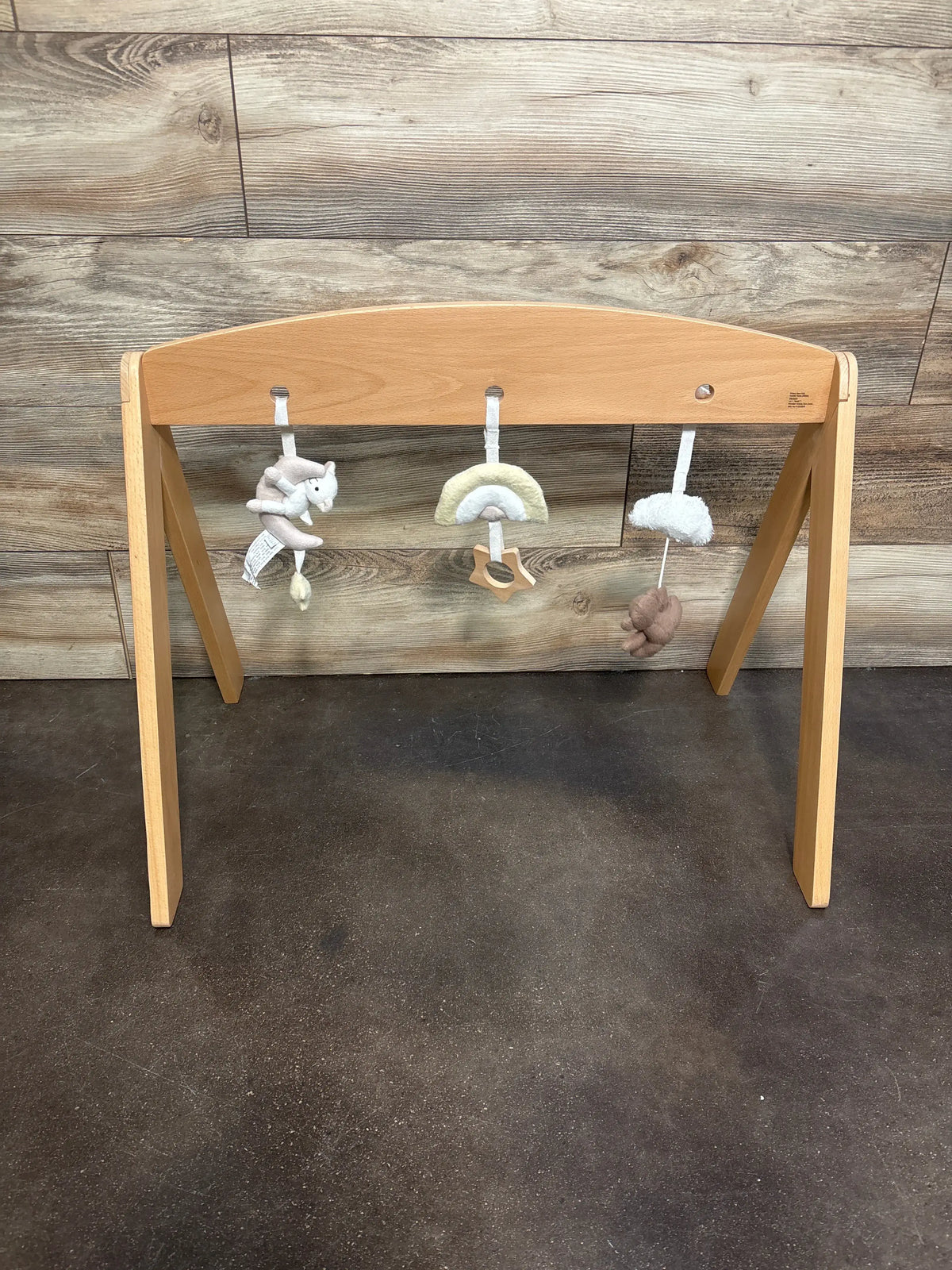 Front view of Pottery Barn Kids Wooden Activity Gym with wooden arch and three hanging toys against wood-look wall