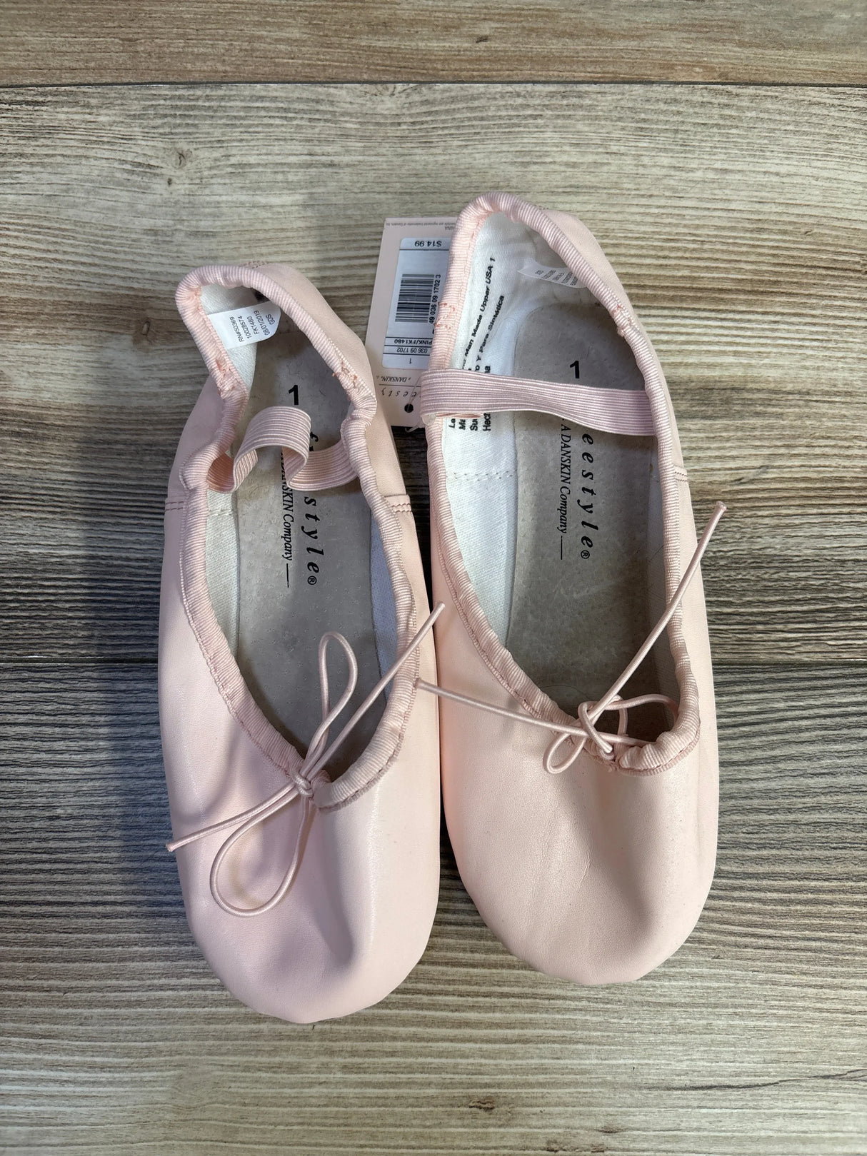 Pink ballet slippers with bows on wooden floor, dance shoes with tags visible