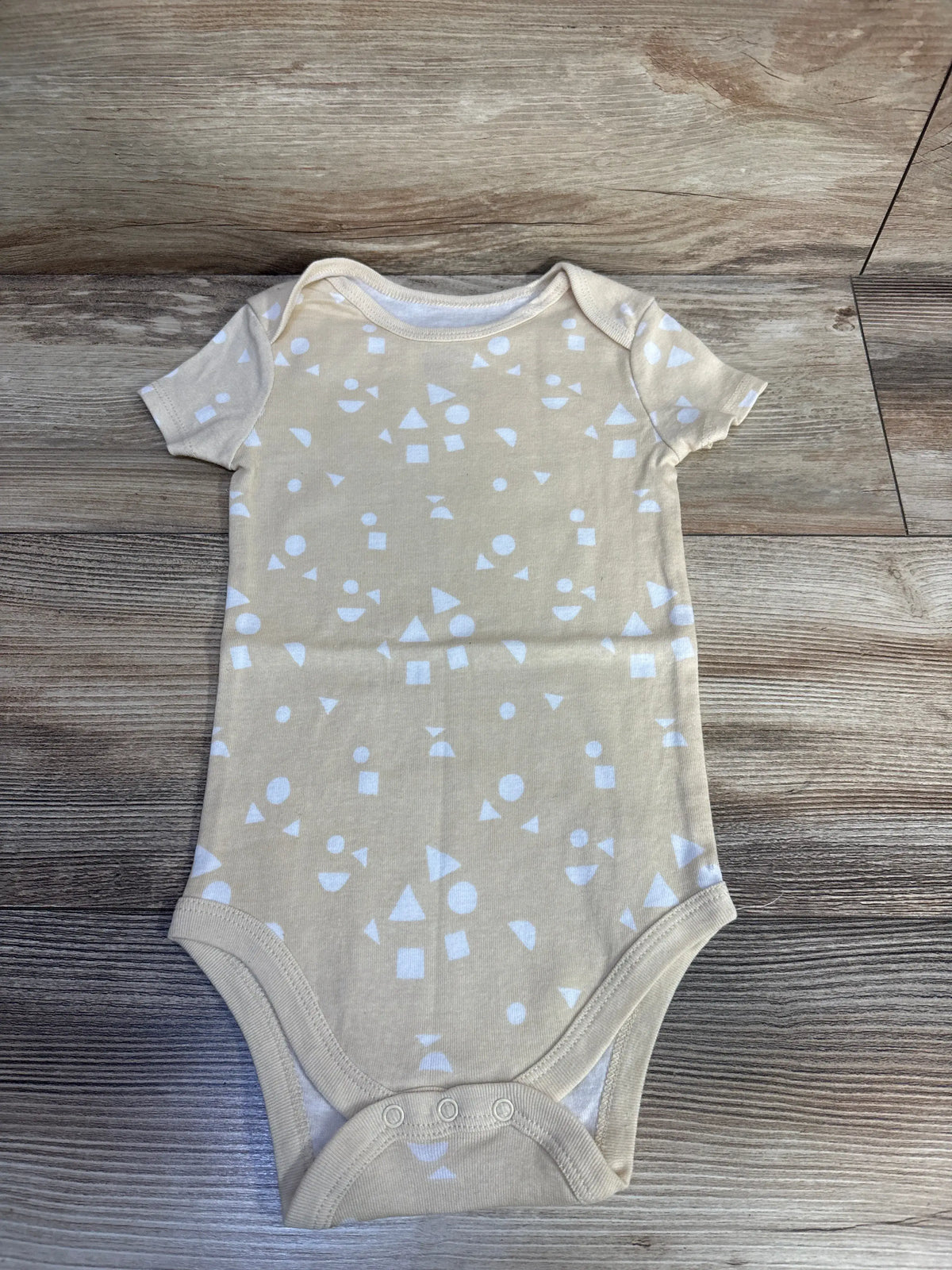 Front view of Okie Dokie pale yellow bodysuit showcasing short sleeves and white geometric pattern on a wood floor