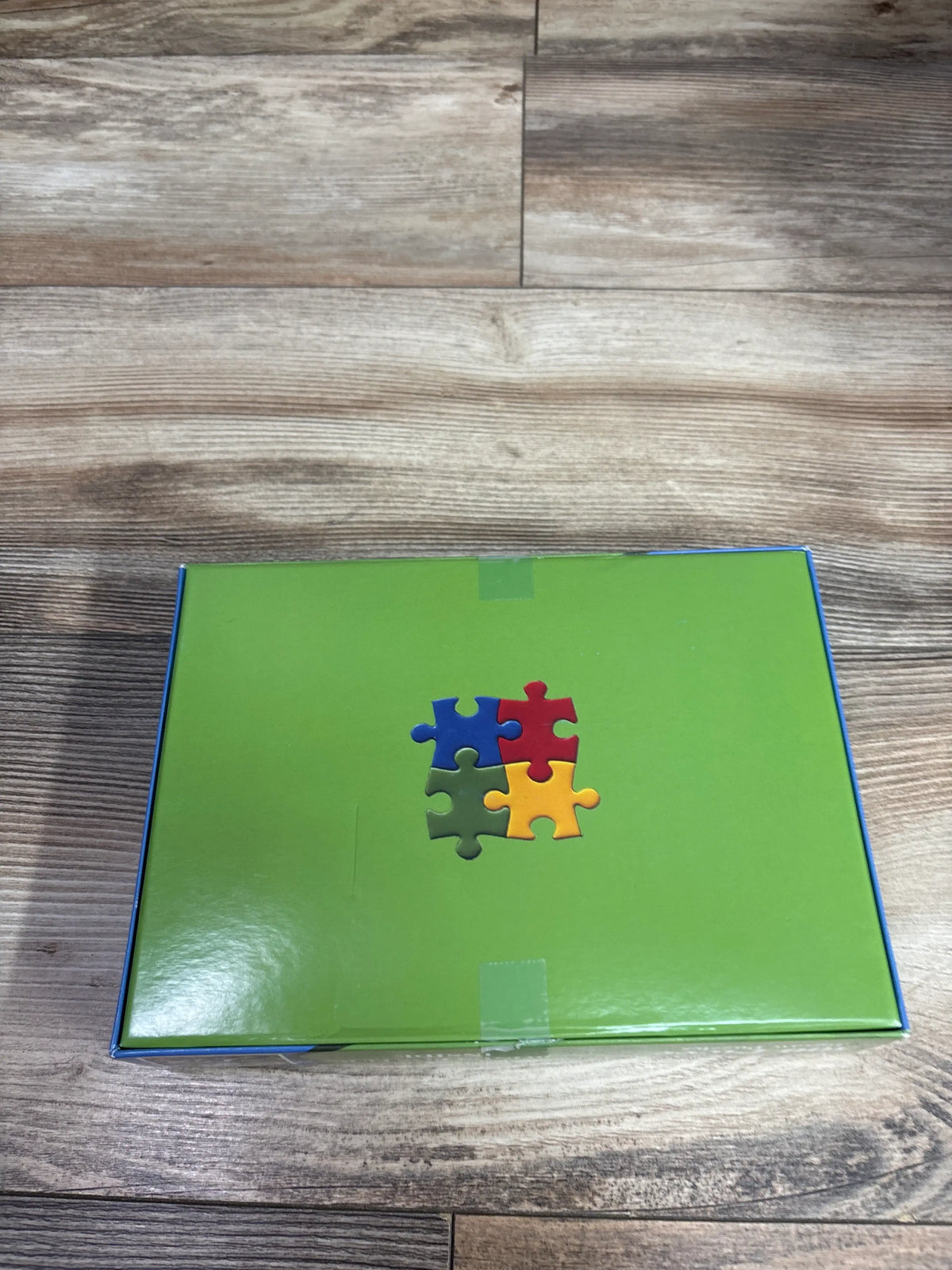 Front view of zhiseoyi 300pc Happy Puppies jigsaw puzzle box showcasing a green cover with colorful puzzle pieces on a wood surface