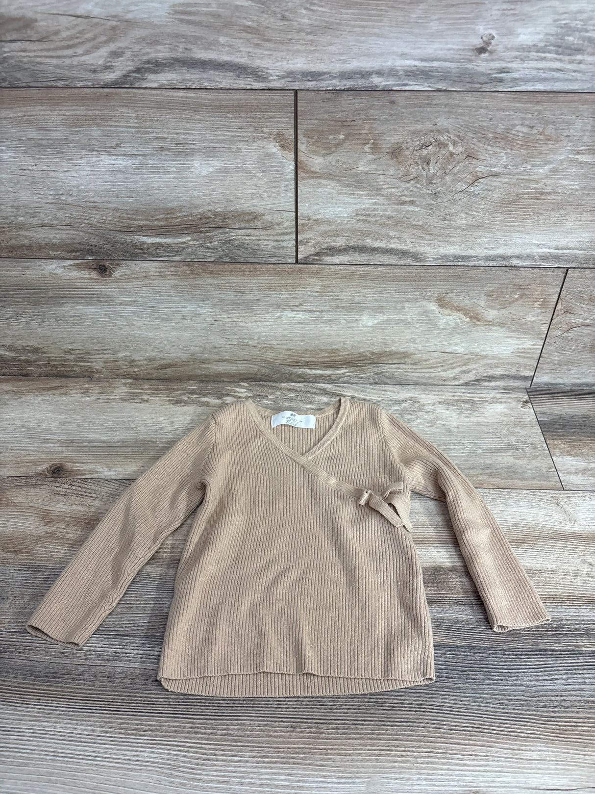 Top-down view of H&M tan fine-knit wrap-front cardigan 3-4T showing ribbed texture and side tie on wood floor