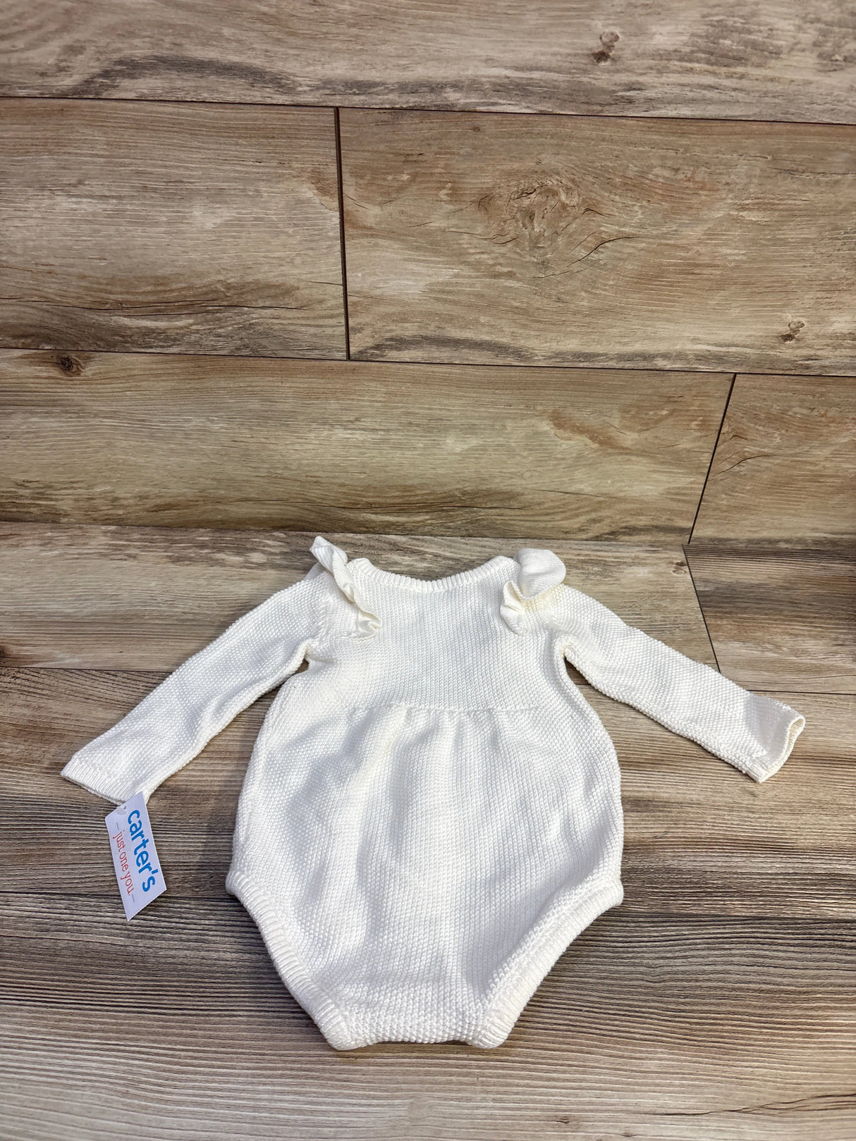 Flat lay of white baby bubble romper with sweater knit, ruffle shoulders and long sleeves, size 9M, on wood floor